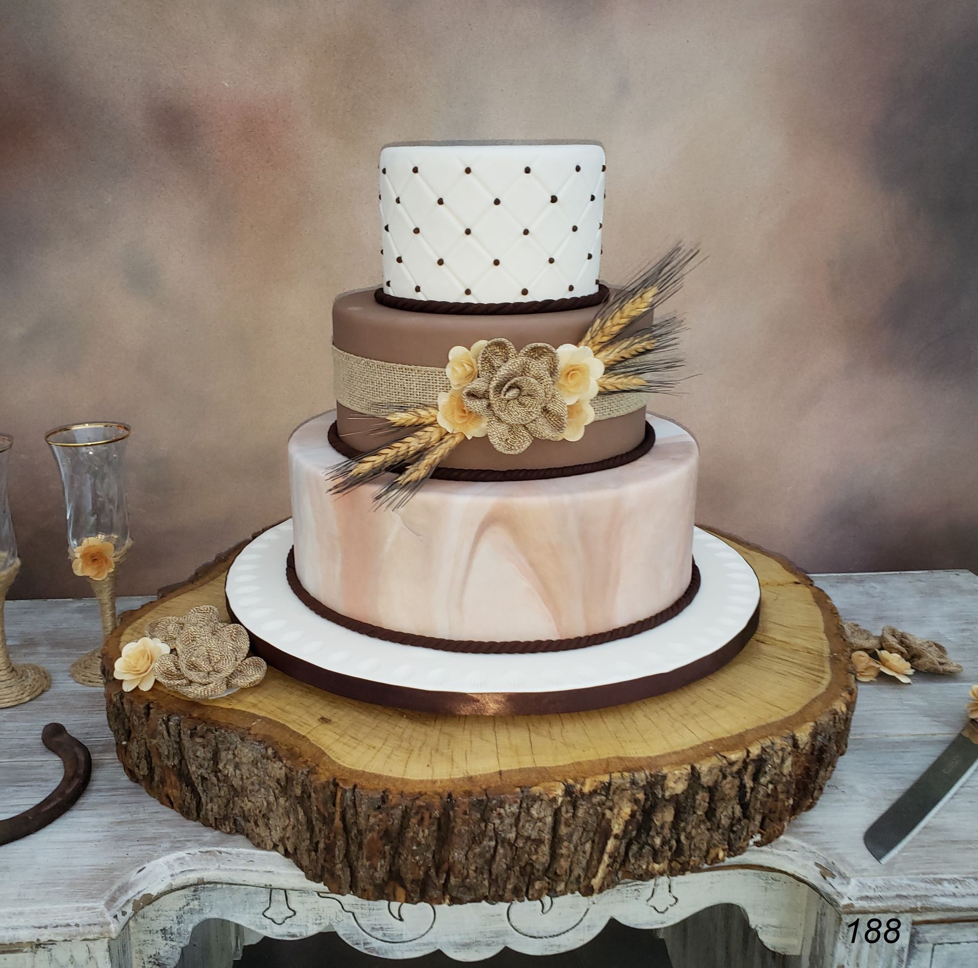 Three-tier rustic cake with wood slice base, cream and beige frosting, and dried floral decorations
