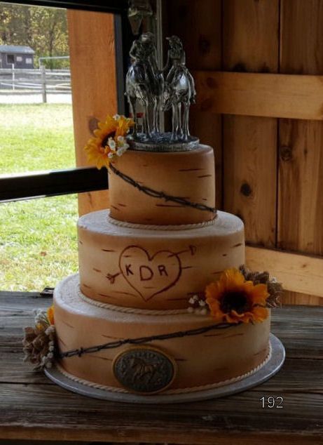 Three-tier white wedding cake with black swirls, sunflowers, and silver bride and groom topper by a window