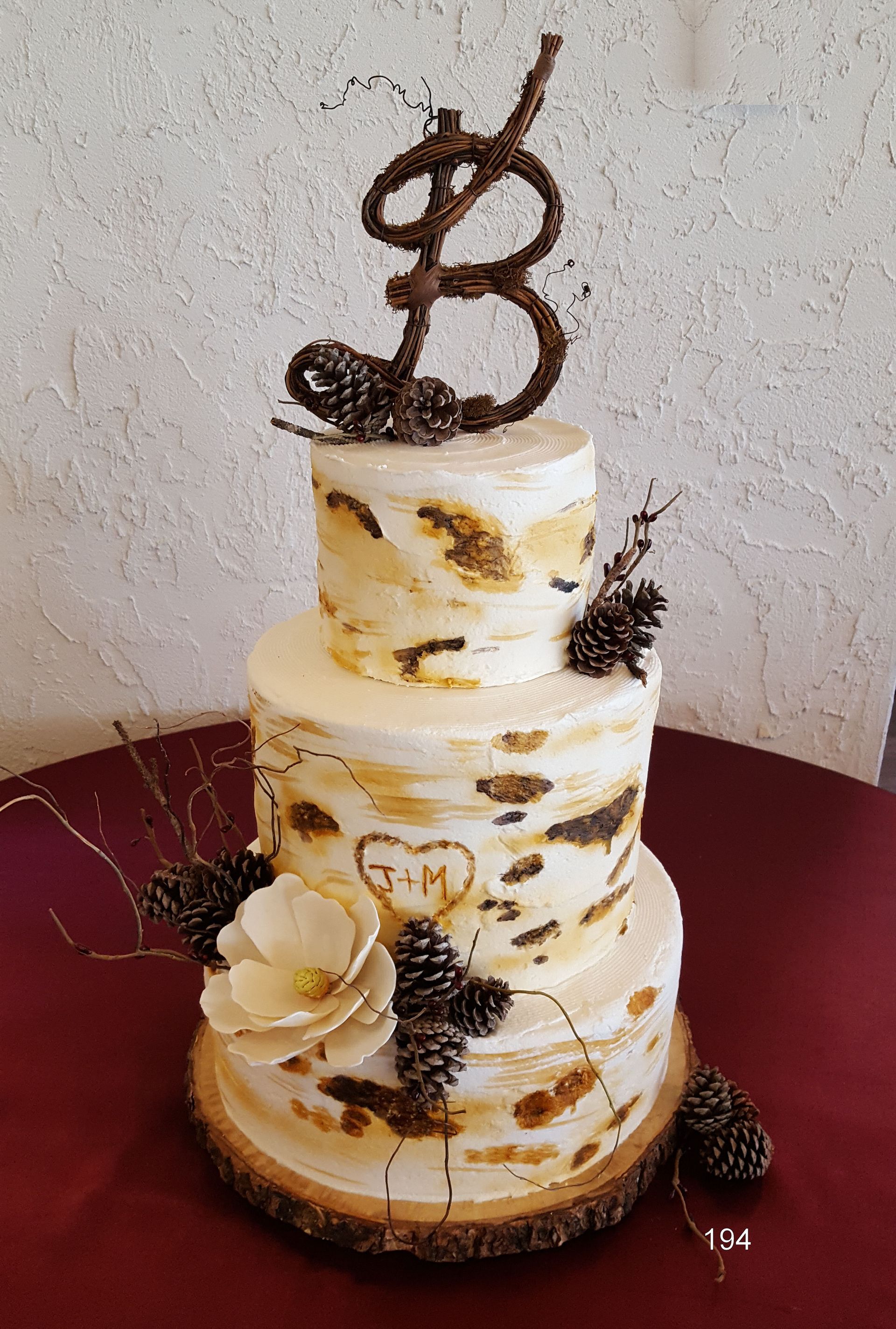 Three-tier white and gold cake with chocolate “8” topper and floral decorations on a burgundy table.