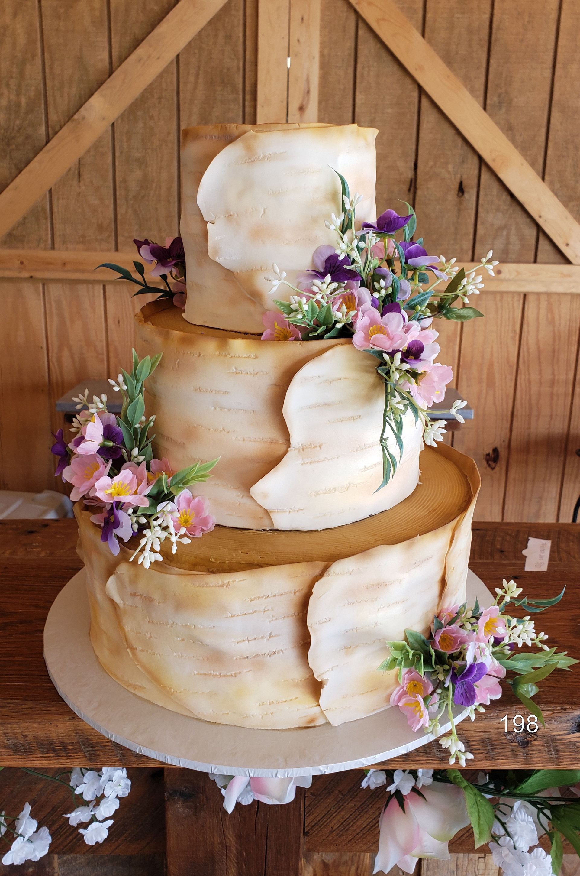 Three-tier rustic white cake with purple flowers and greenery on a wooden table