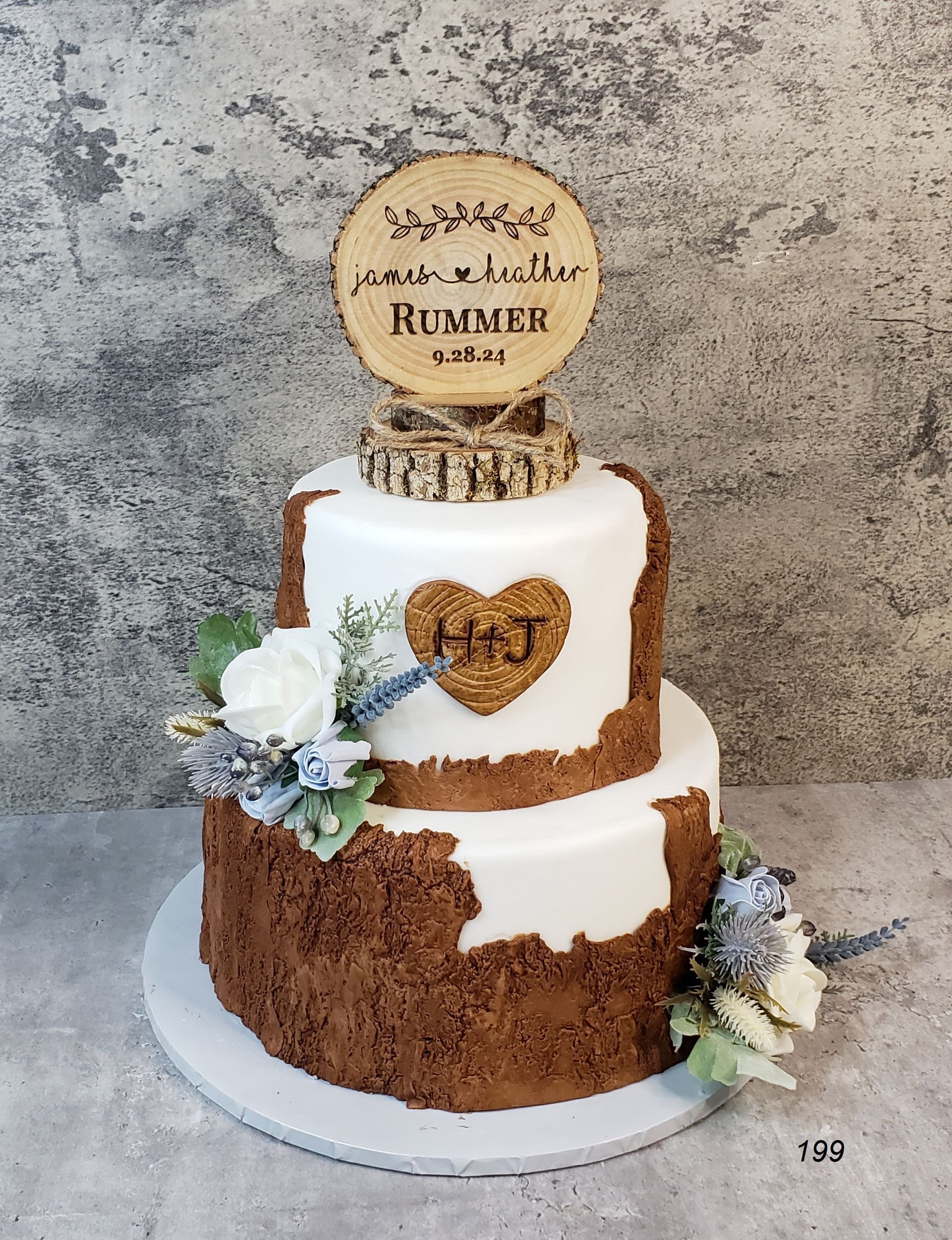 Two-tier white and gold birthday cake with floral accents and a topper reading “Remember” on a round stand