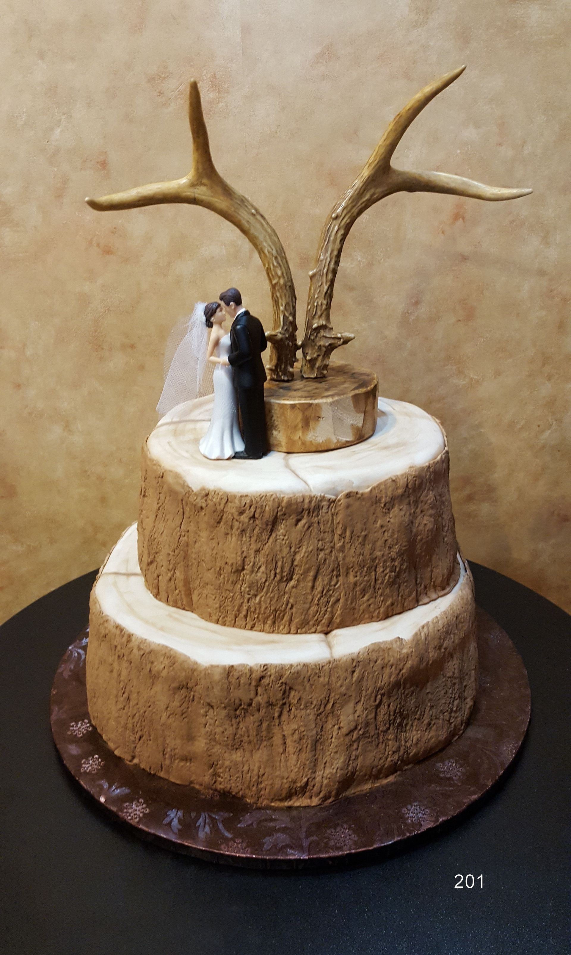 Two-tier rustic cake with white icing, deer antlers, and a small couple figurine topper