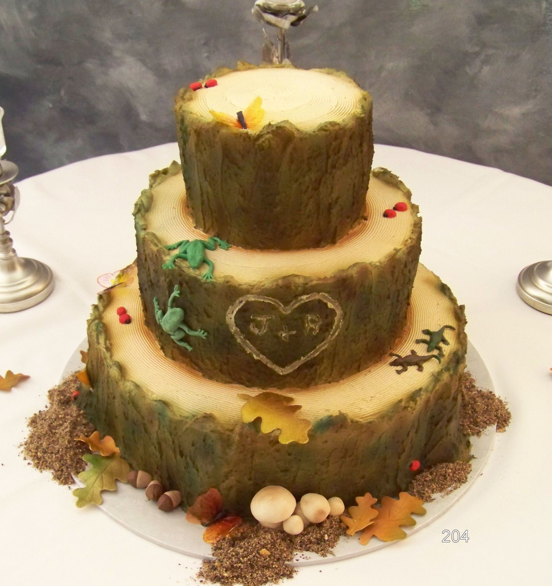 Three-tier rustic tree-stump cake with autumn leaves and heart decoration on a white platter