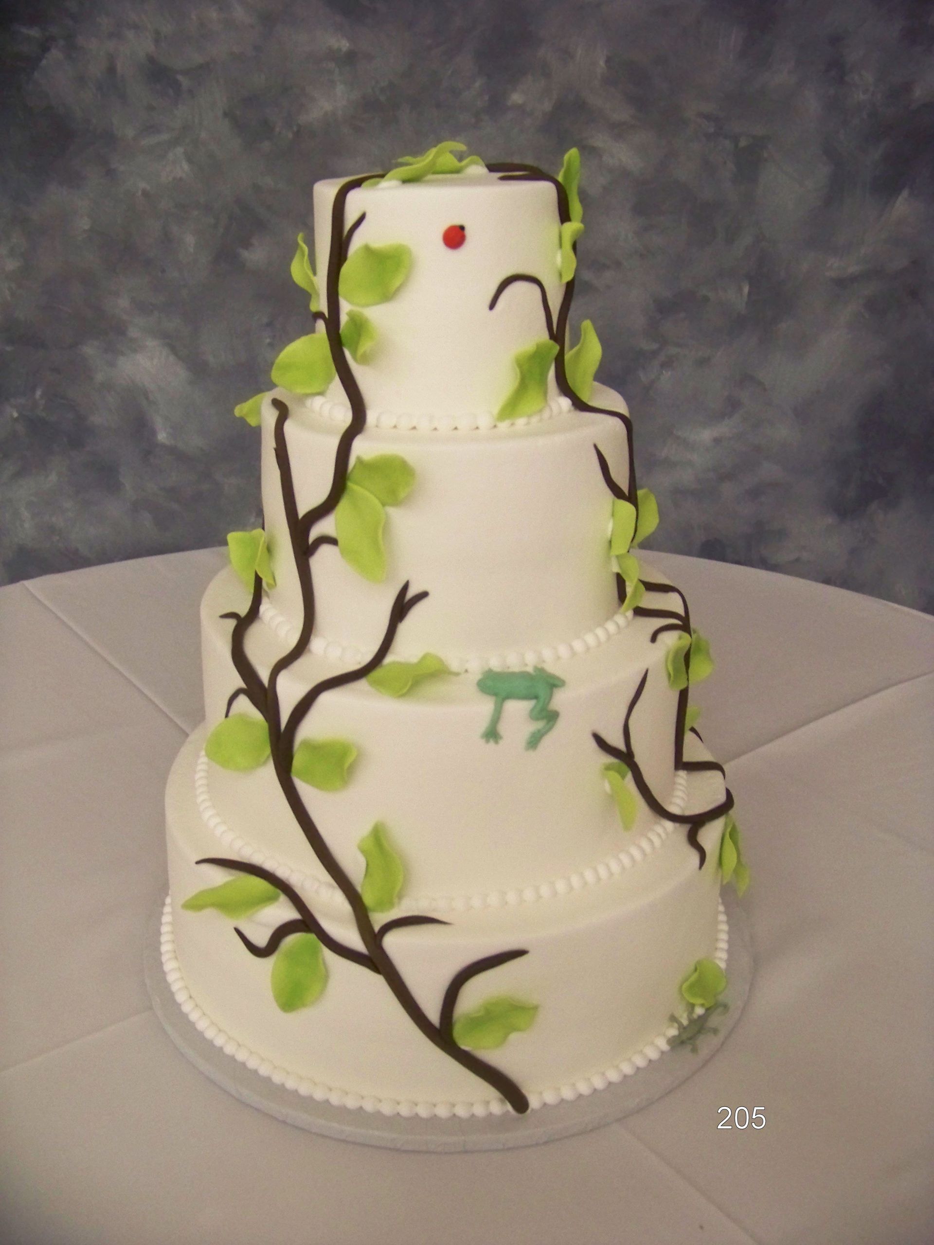 Three-tier white cake with green vine and leaf decorations on a gray backdrop