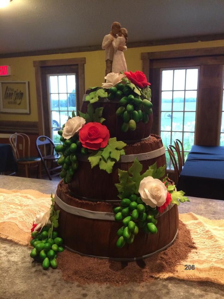 Three-tier chocolate wedding cake with pink and white roses, green leaves, and a bride and groom topper