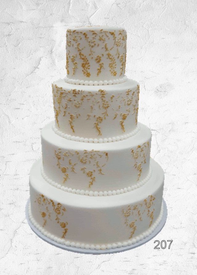 Four-tier white wedding cake with gold leaf accents on a white textured background