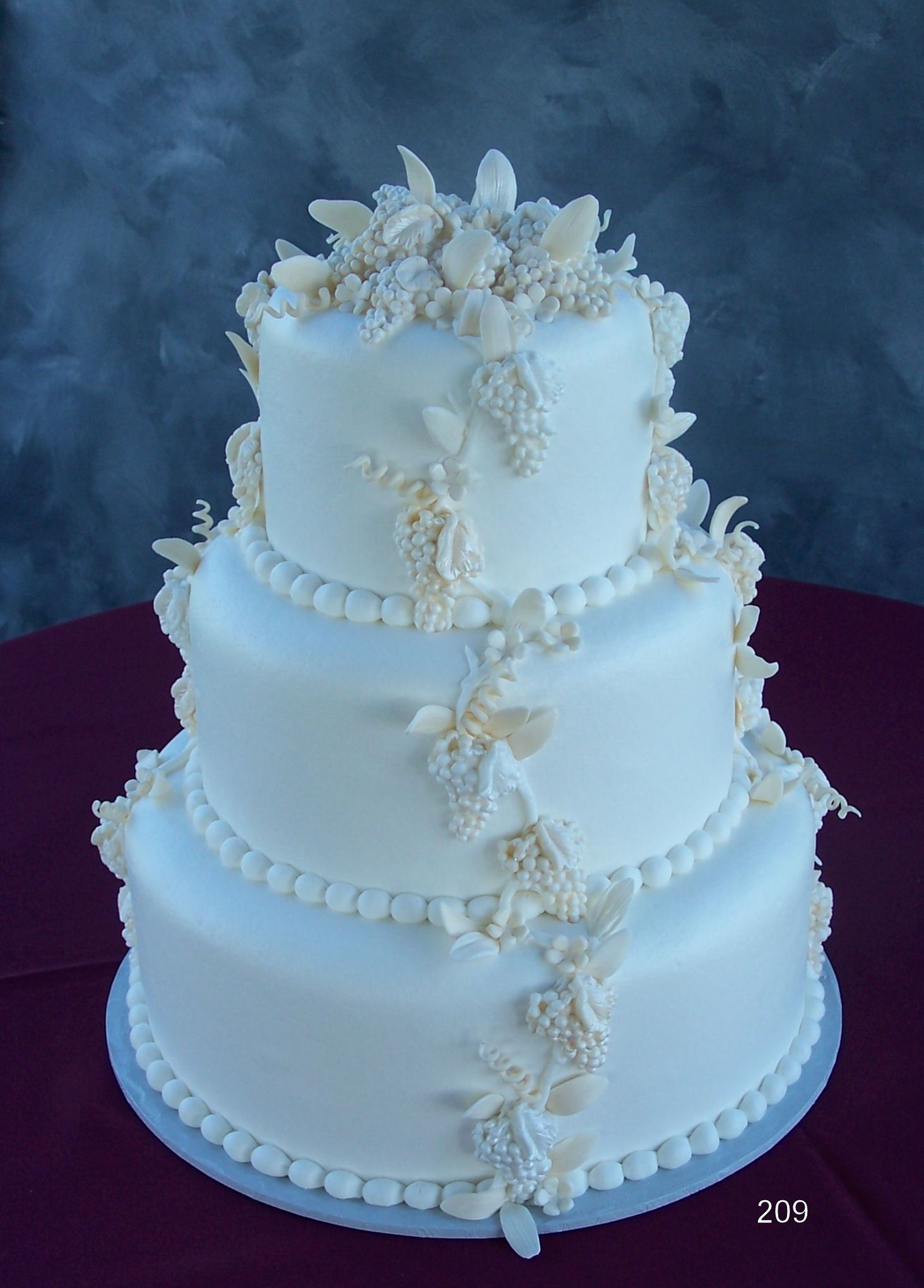 Three-tier white wedding cake with floral decorations and beaded trim on a dark backdrop