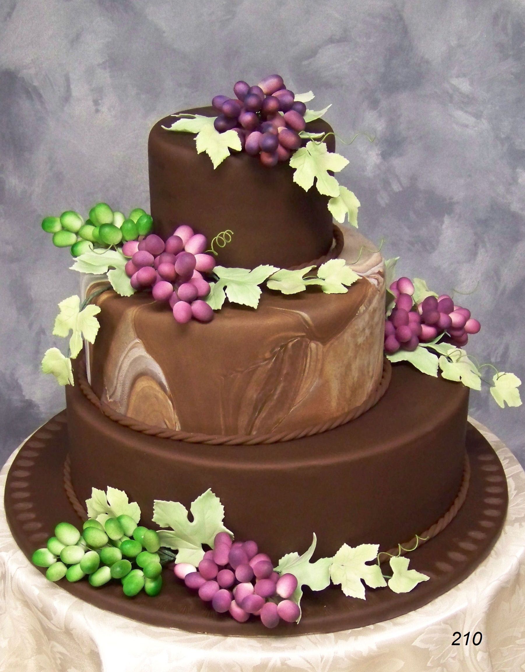 Tiered chocolate cake with purple and green grape decorations on a white plate