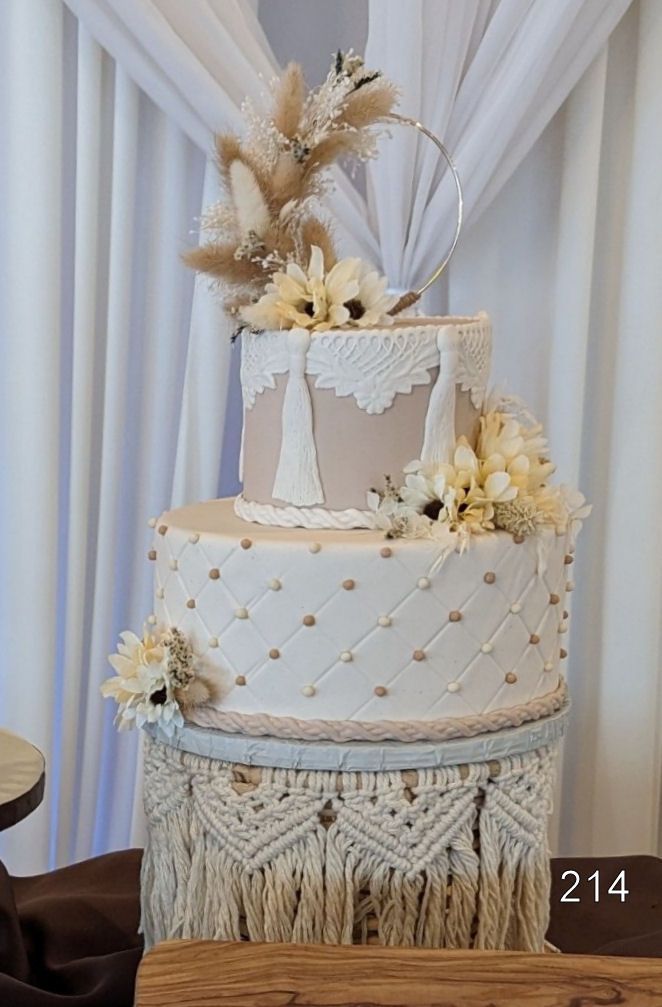Three-tier cream and gold decorated cake with dried flowers and lace details on a dessert table