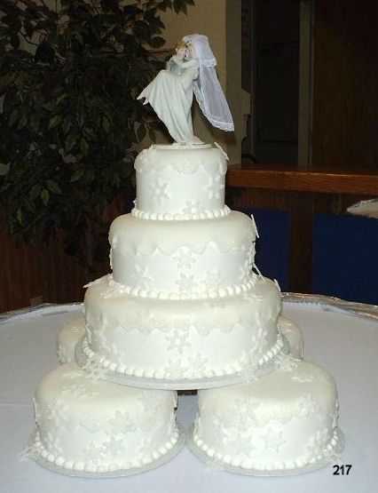 White four-tier wedding cake with a small bride and groom topper on a table