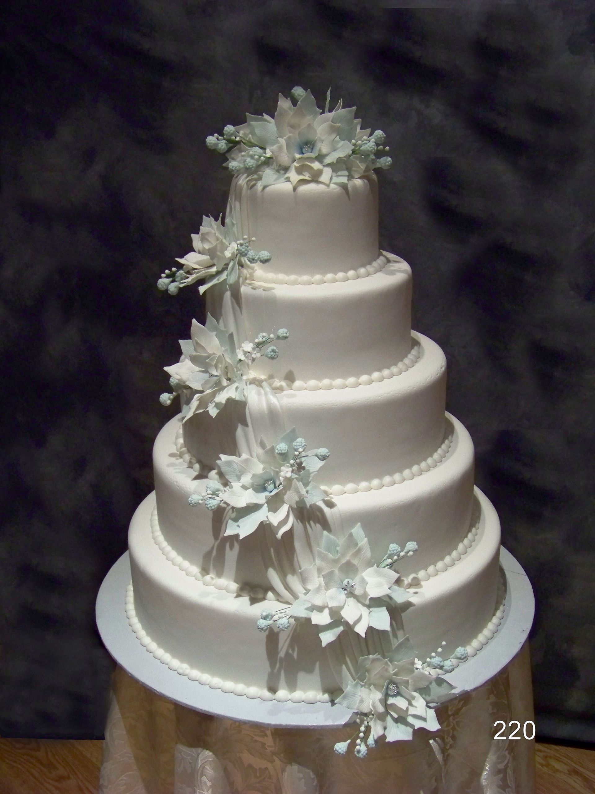 White tiered wedding cake with cascading pale blue and white flowers on a scalloped cake board
