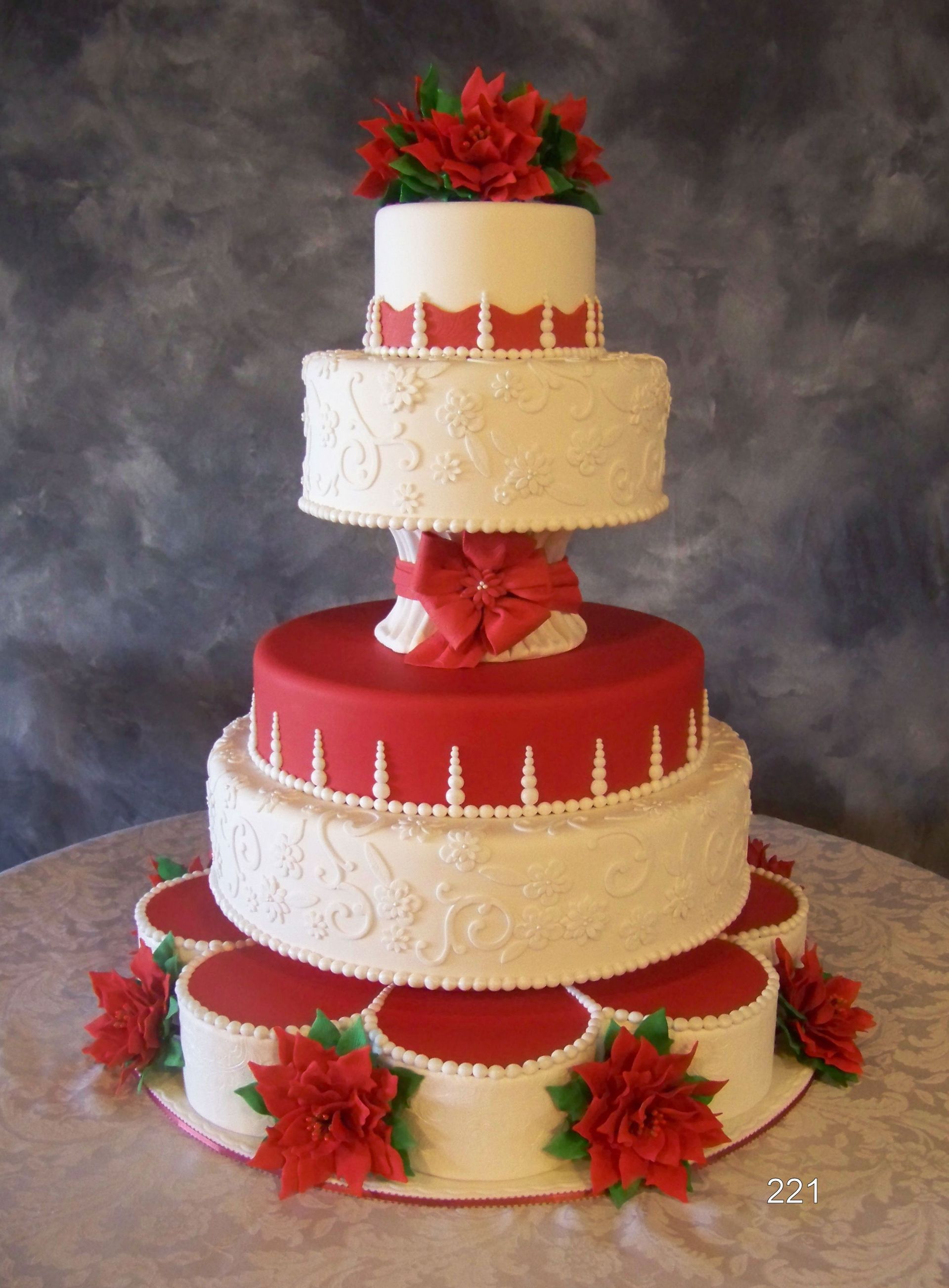 Four-tier white and red wedding cake with floral decorations on a table