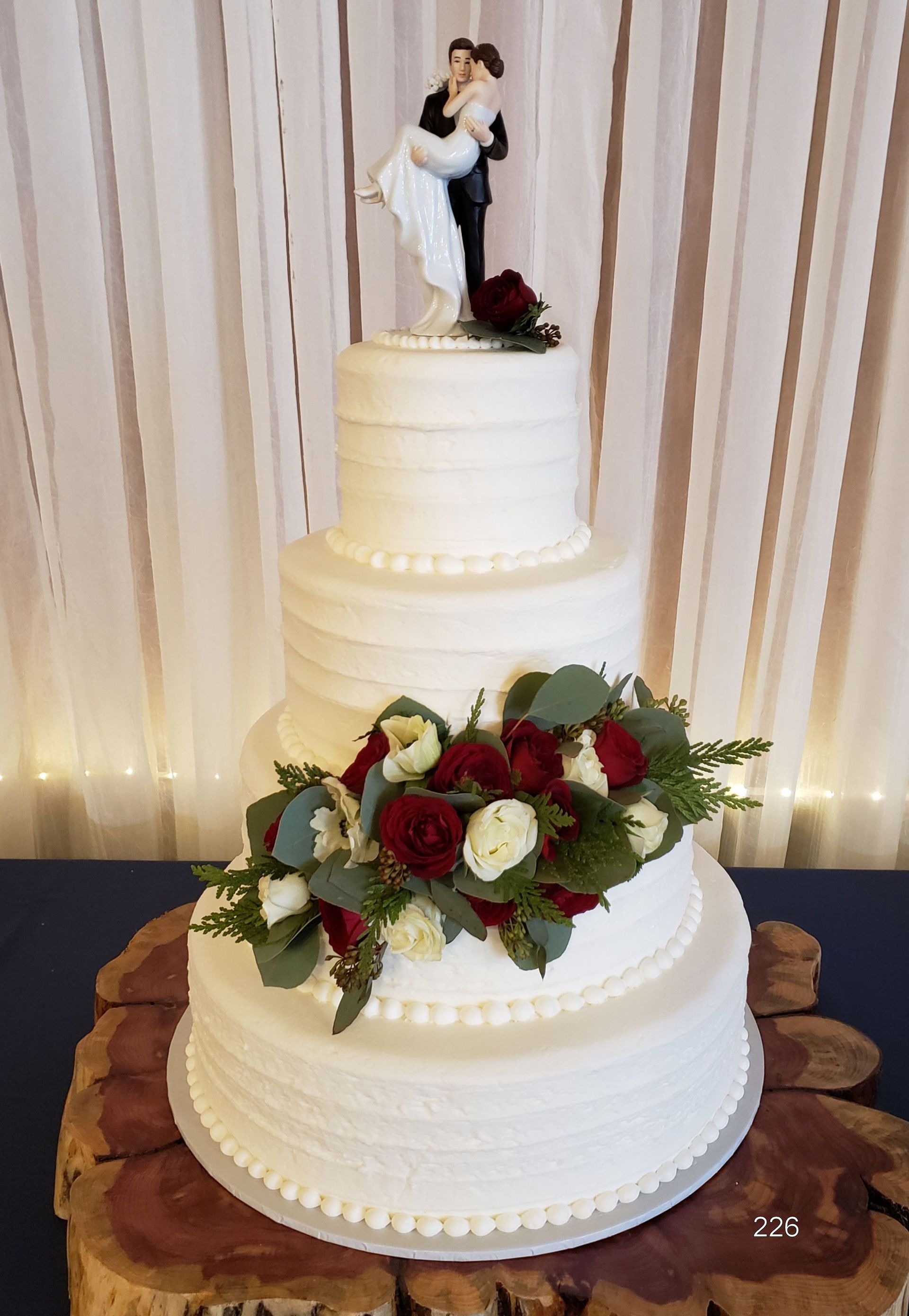 Two-tier white wedding cake with red and white roses and a bride-and-groom topper