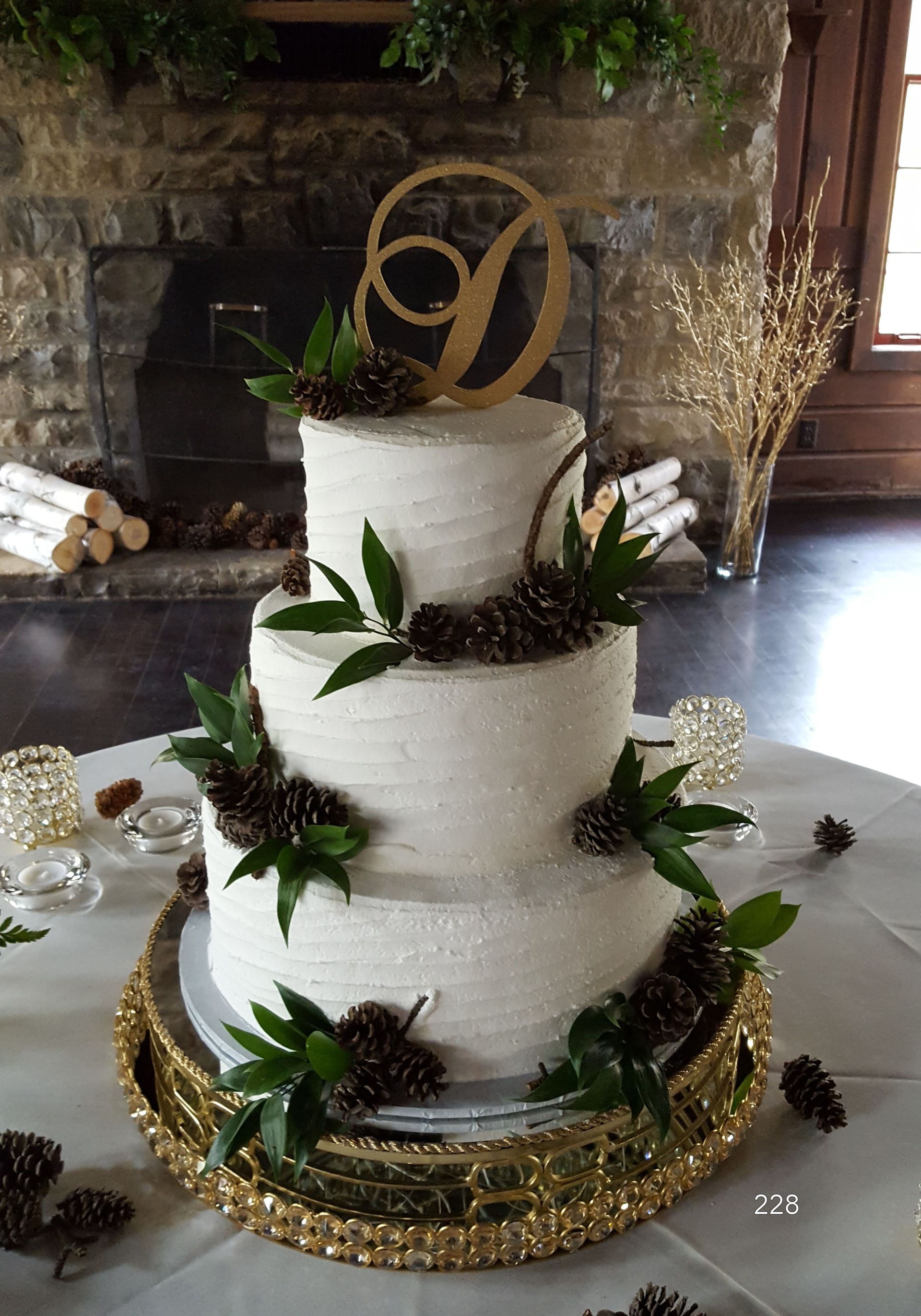 Three-tier white wedding cake with green leaves and gold decorations on a rustic table.