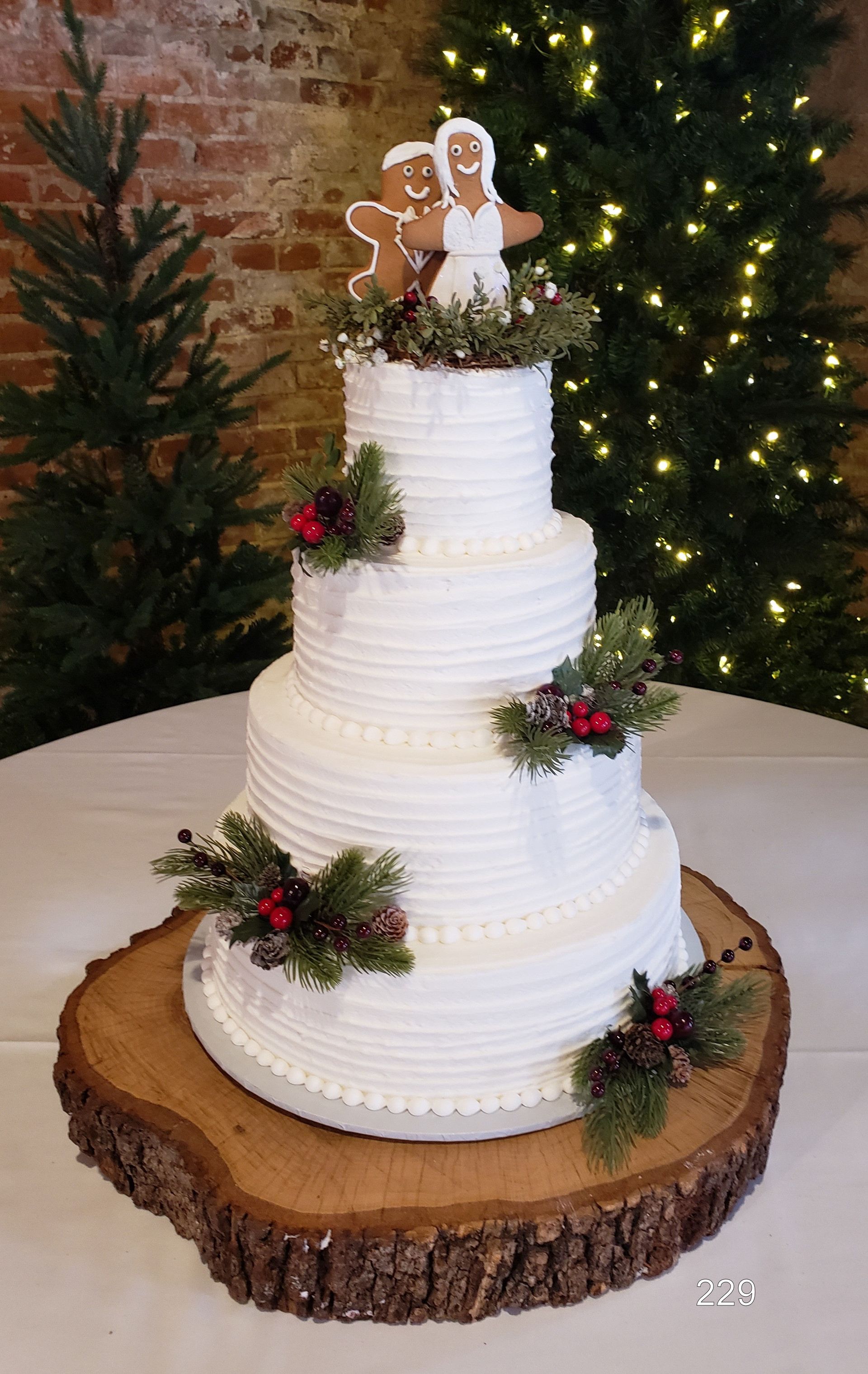 Rustic white tiered wedding cake with greenery and a gingerbread topper on a wood-slice stand
