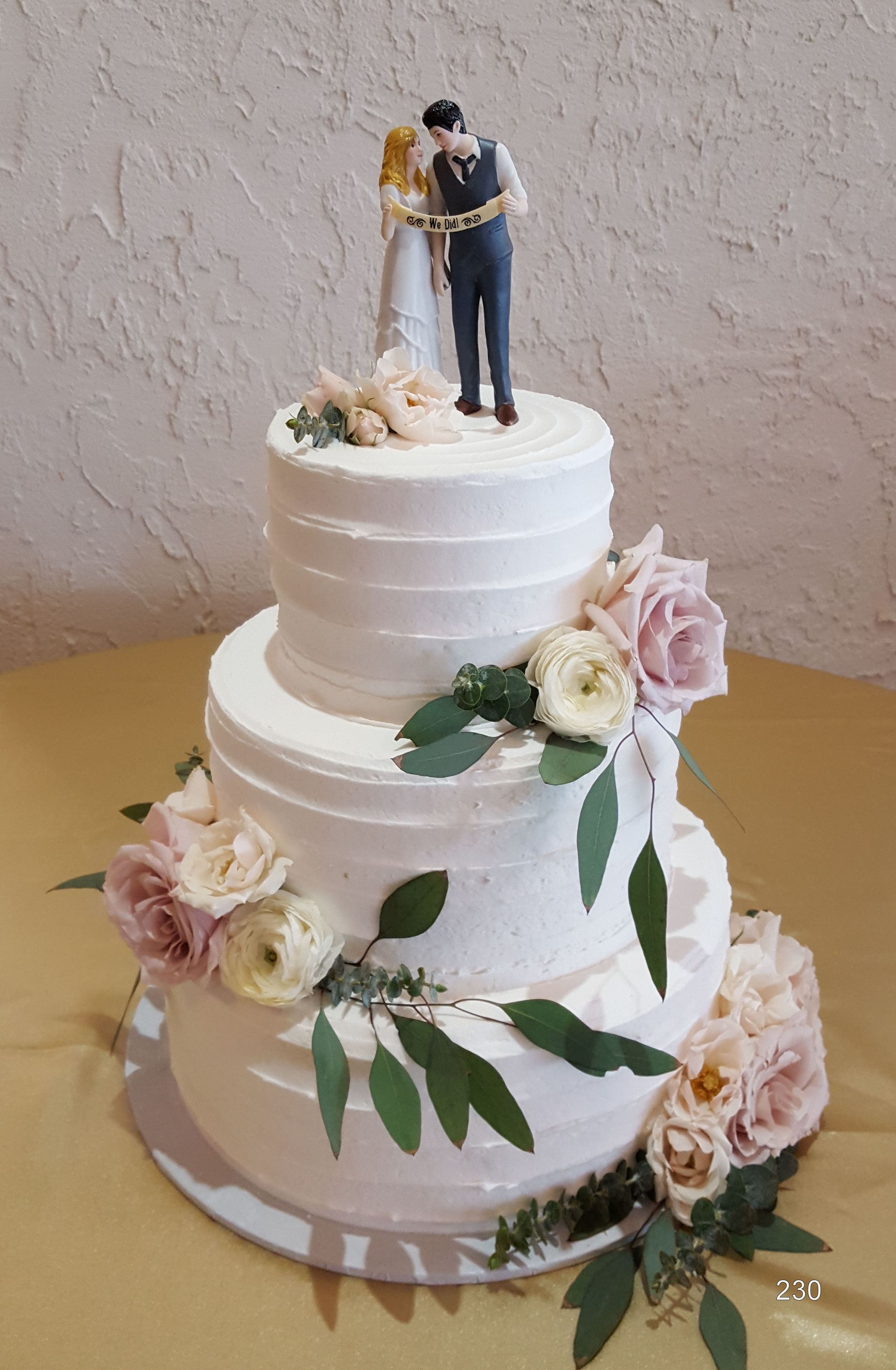 White tiered wedding cake with floral decorations and a bride-and-groom topper