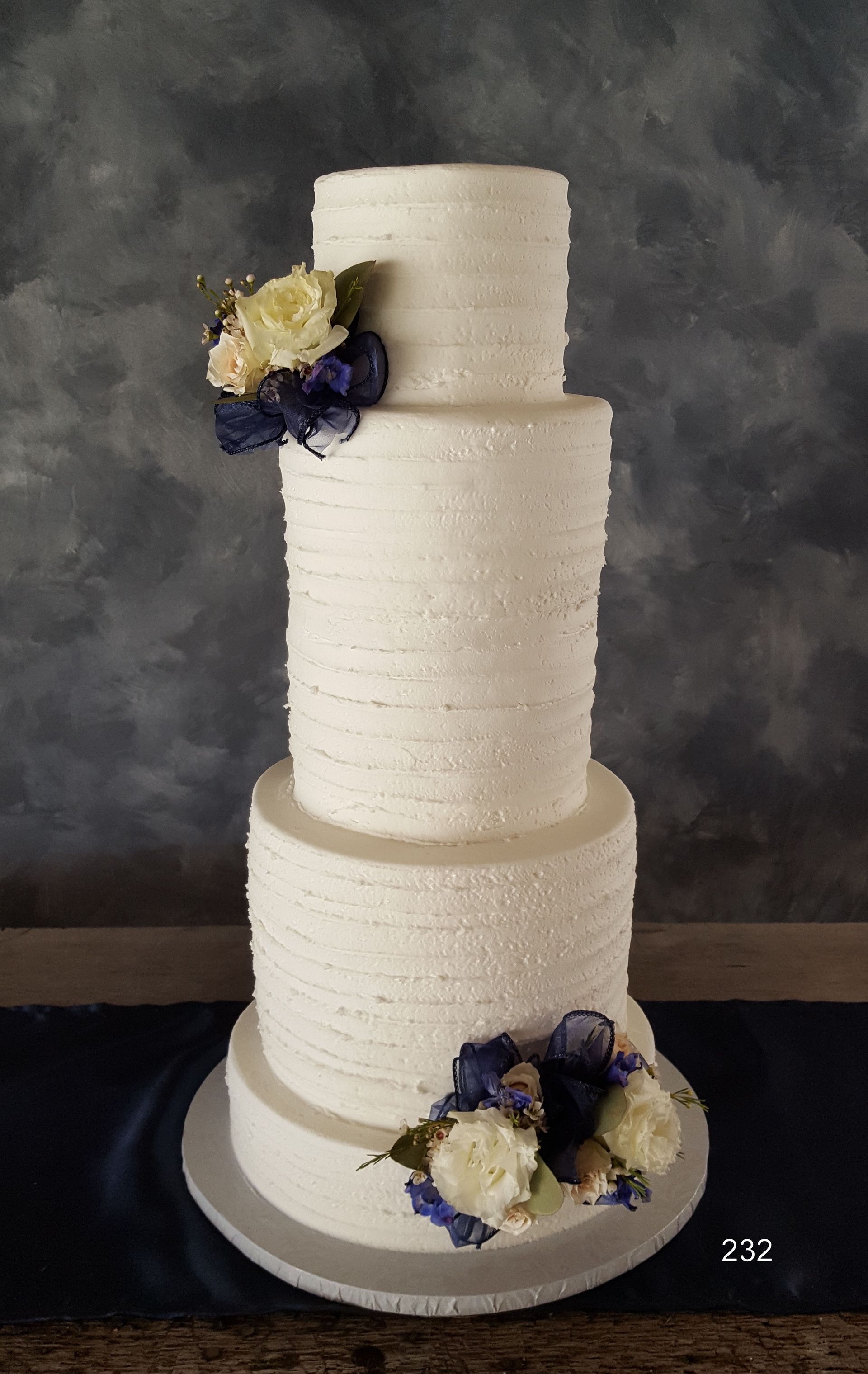Three-tier white wedding cake with navy and cream floral decorations on a dark table.