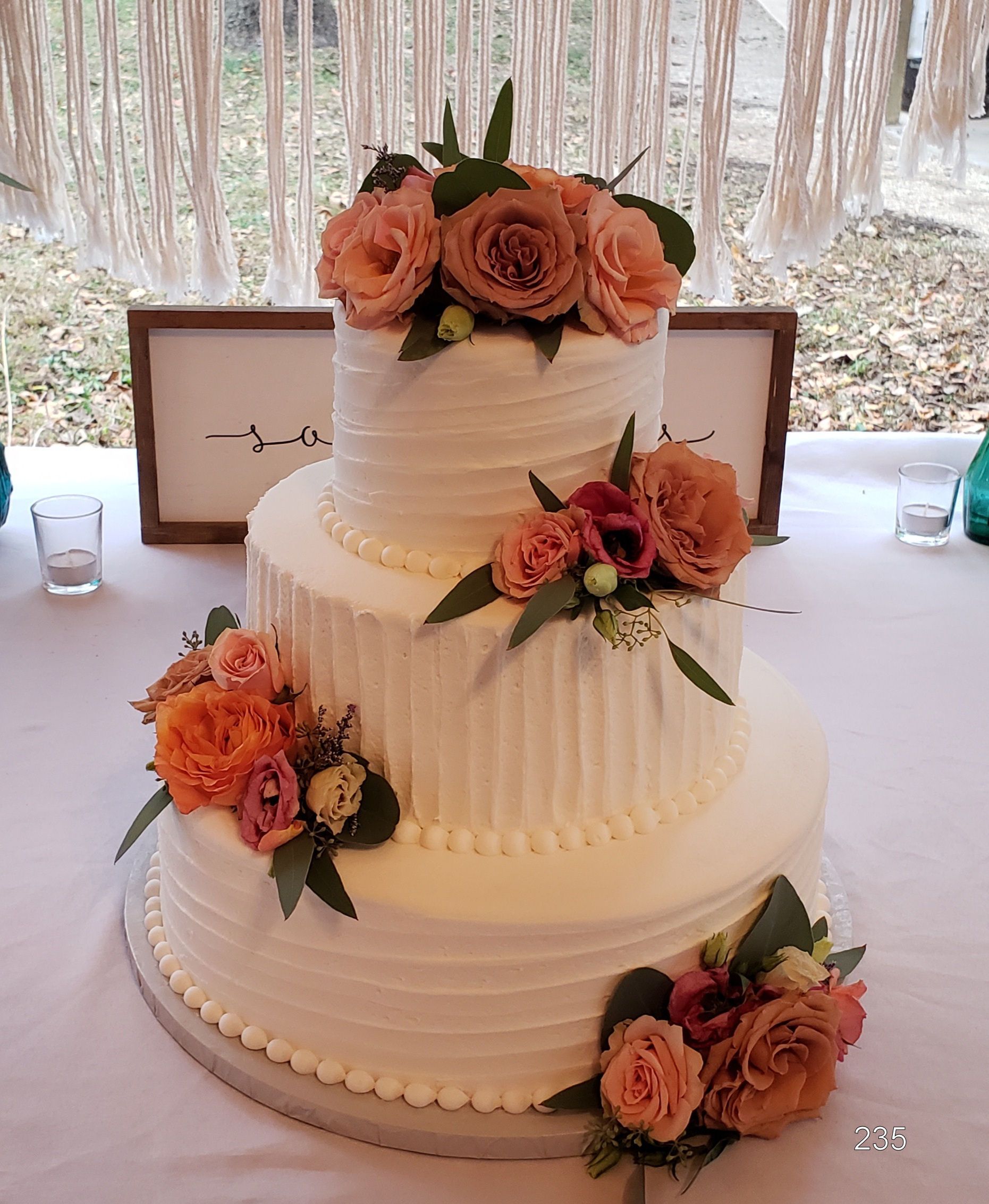 Three-tier white wedding cake with peach and pink floral decorations on a reception table