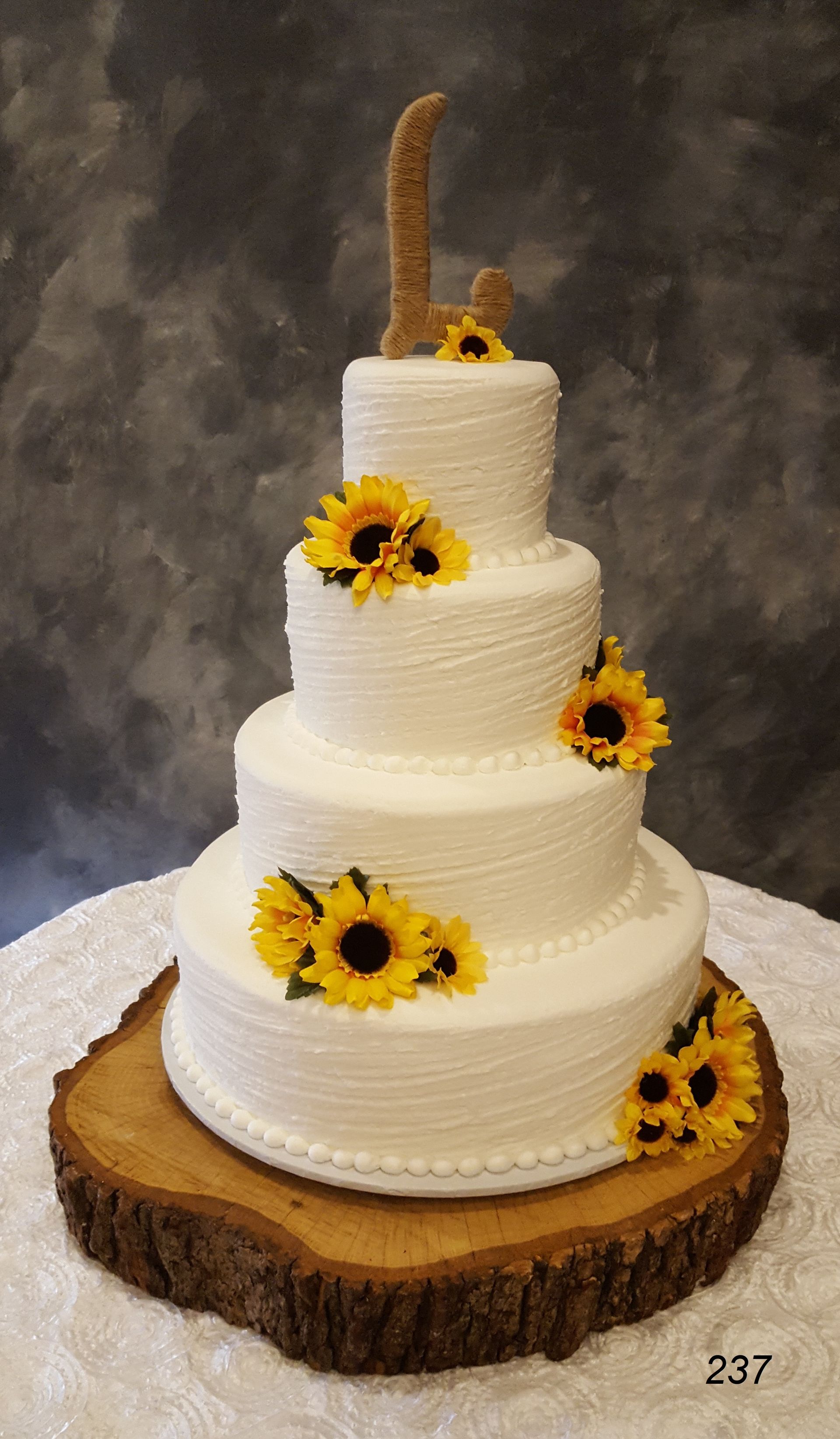 Four-tier white wedding cake with sunflower decorations on a rustic wood slice stand