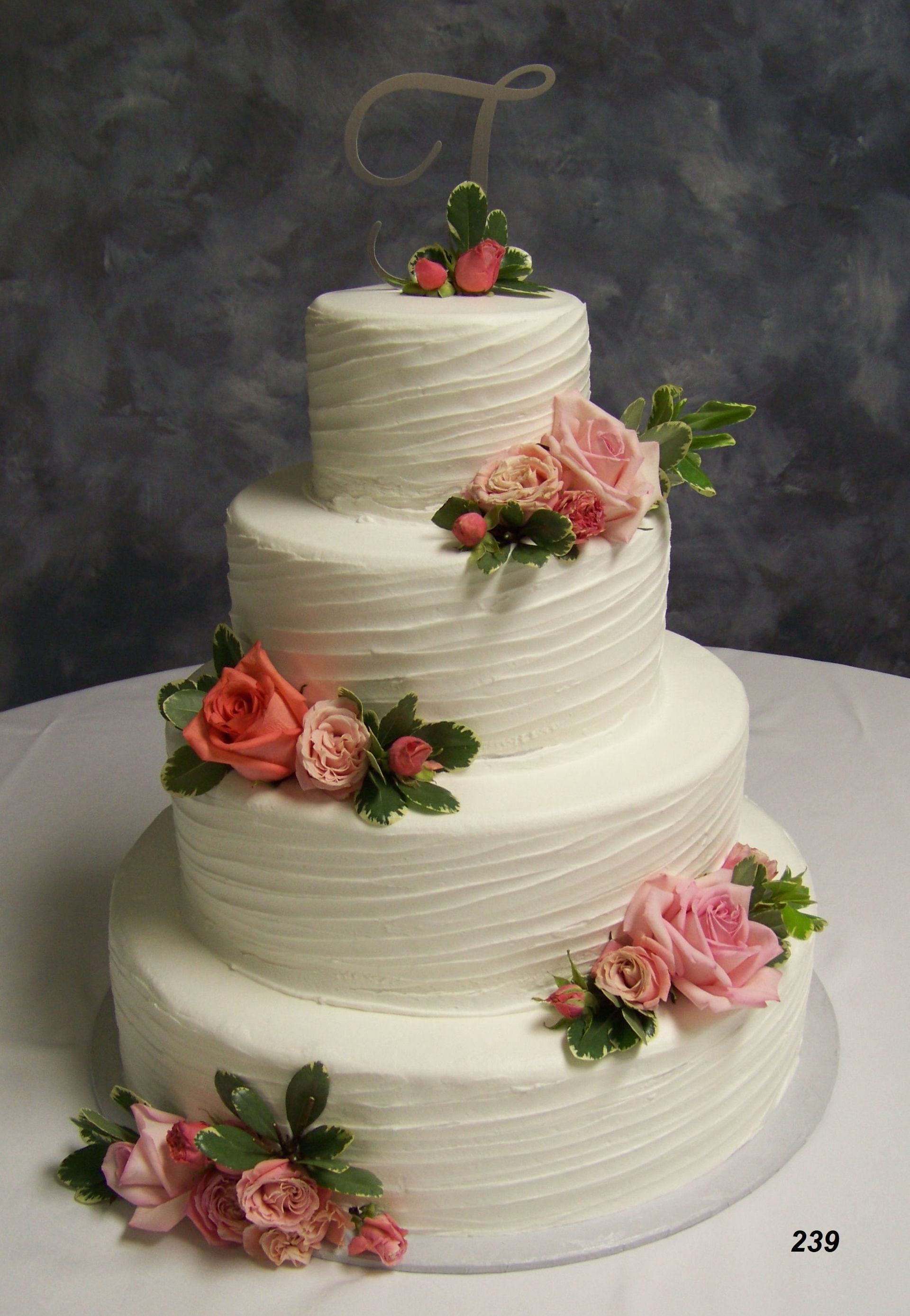 Four-tier white wedding cake with pink and coral floral decorations on a dark backdrop
