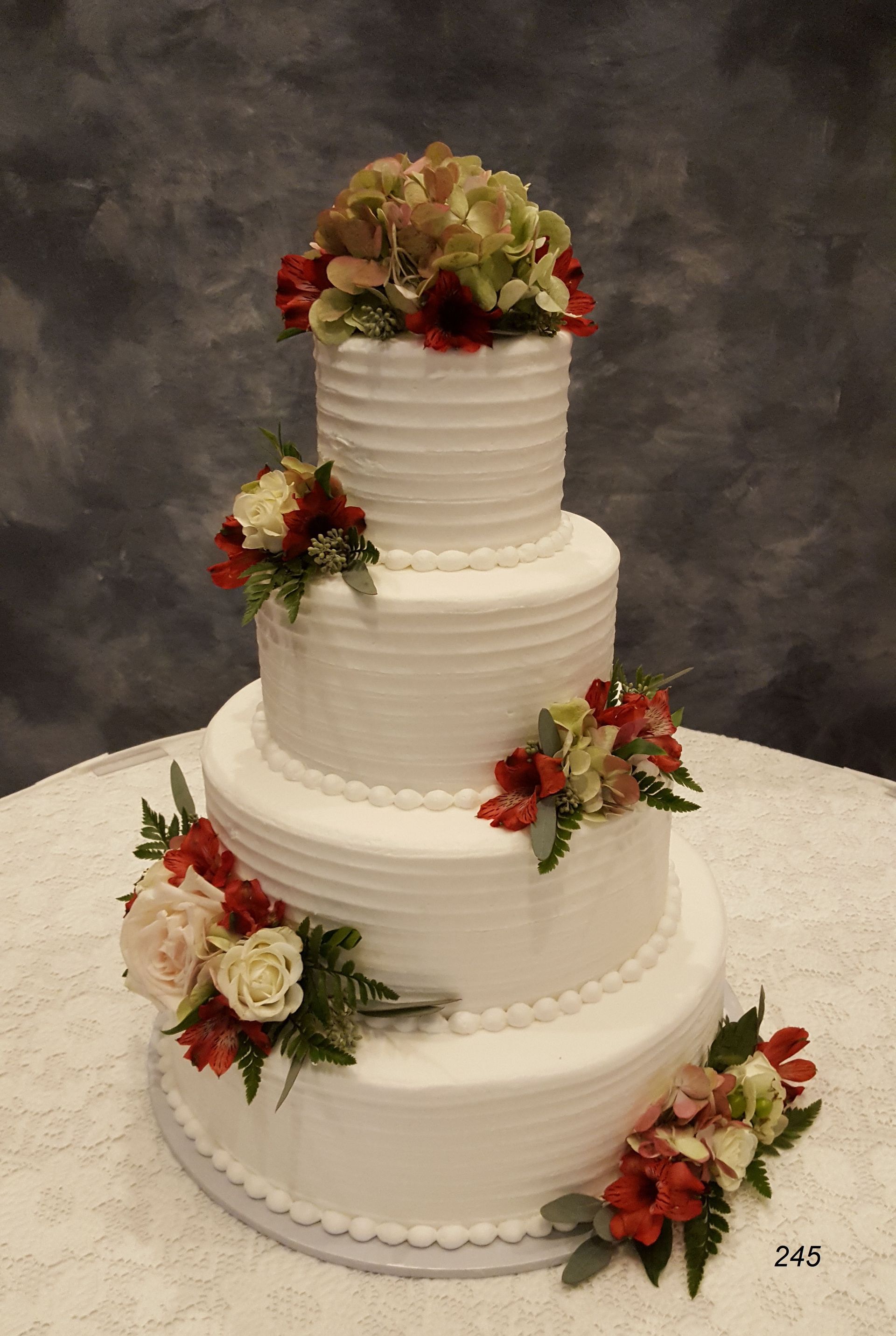 Four-tier white wedding cake with floral arrangements on a round table