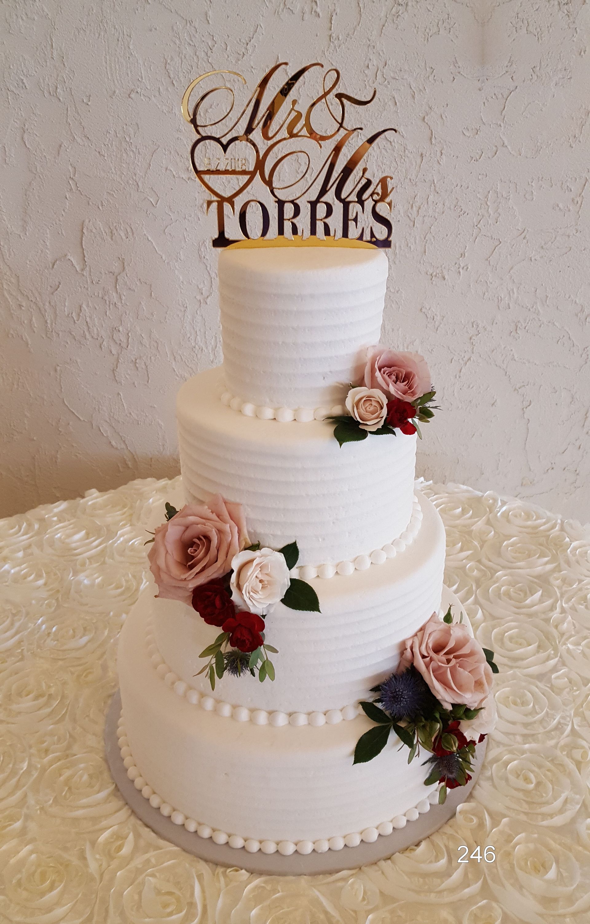 Four-tier white wedding cake with pink roses and gold “Mr & Mrs Torres” topper