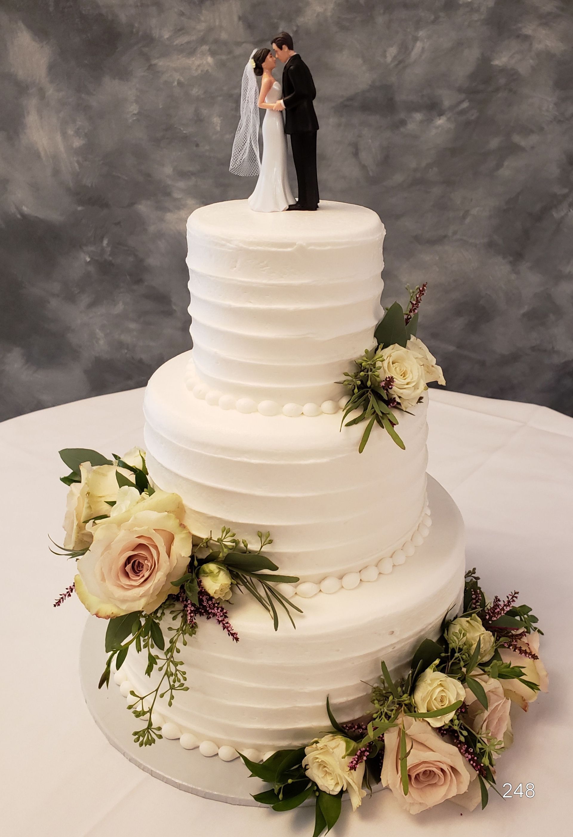 Three-tier white wedding cake with floral arrangements and a bride-and-groom topper