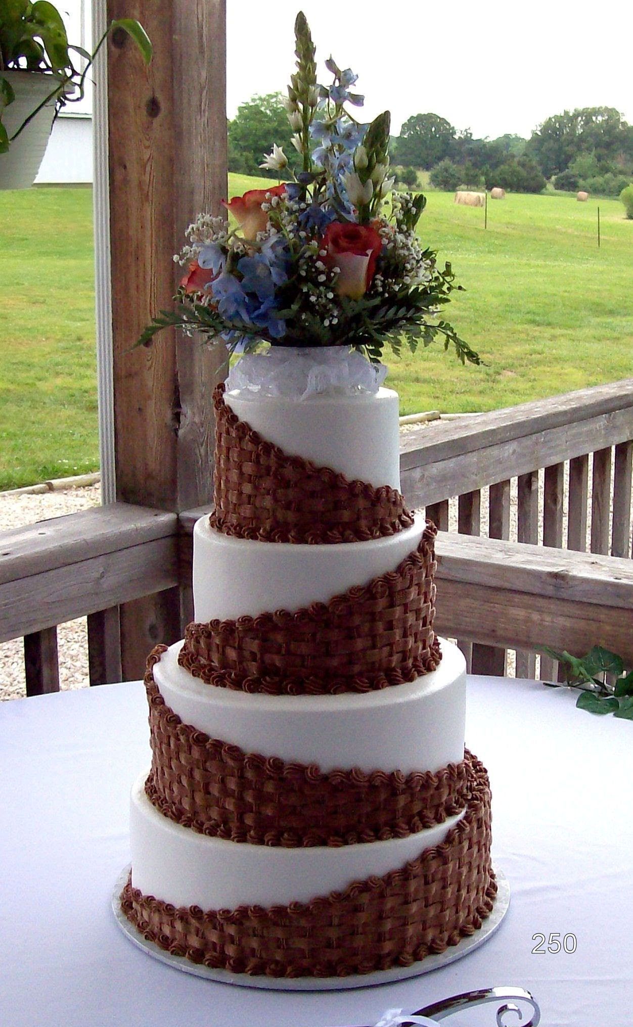 Tall white and brown tiered wedding cake with flowers on an outdoor porch overlooking a grassy field