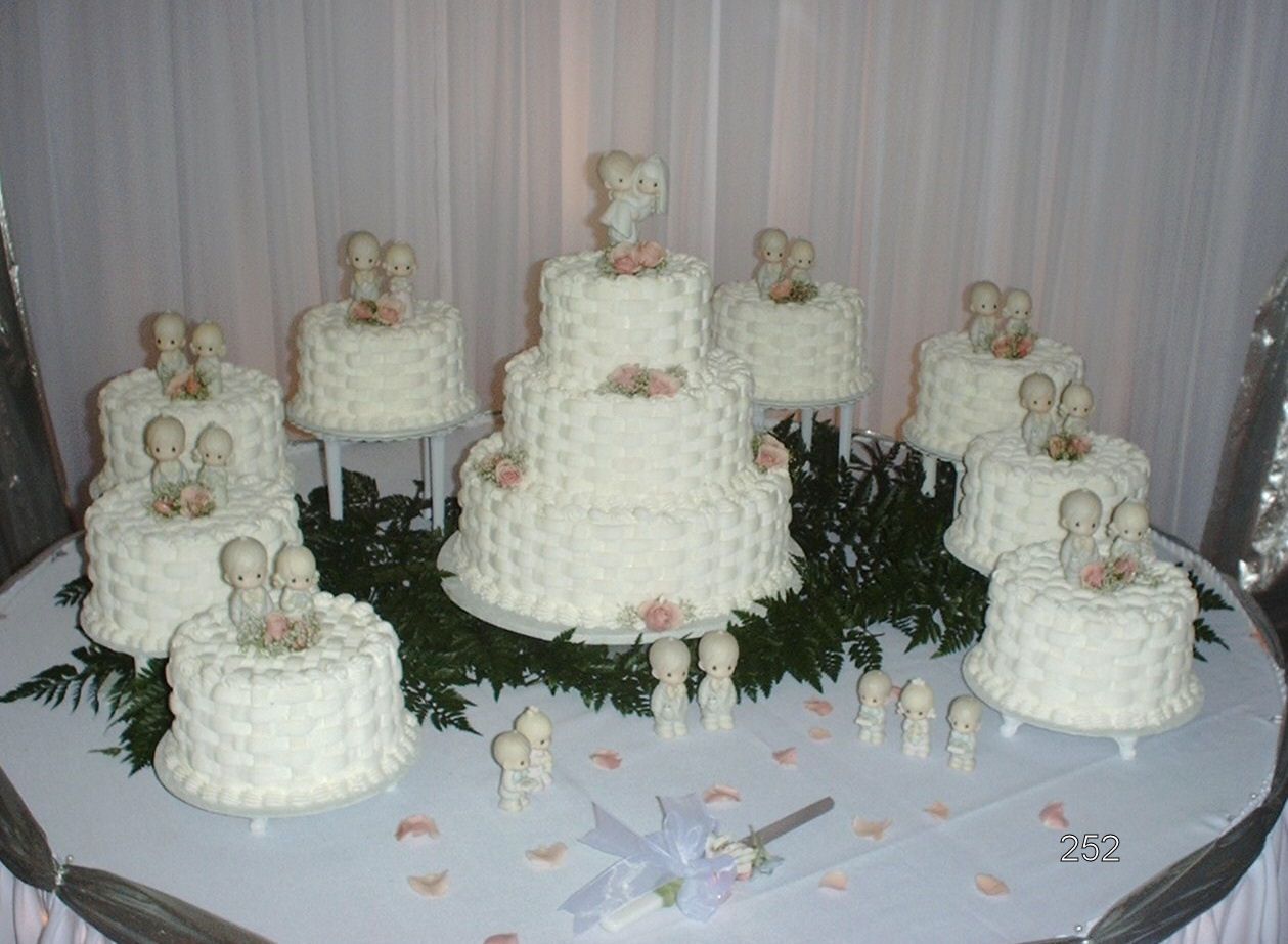 Seven white tiered cakes with figurines on a decorated table at a reception