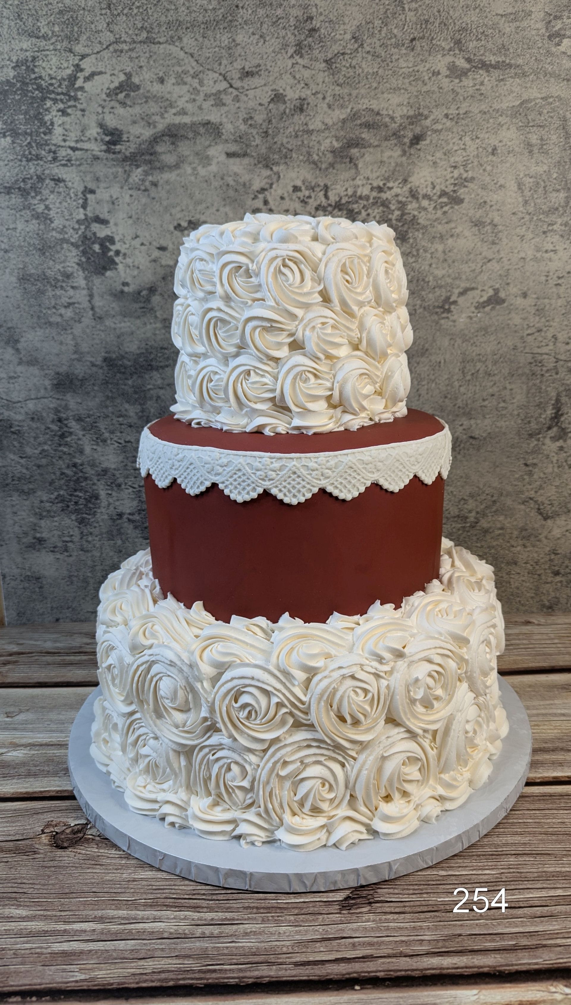 Two-tier wedding cake with white rose frosting and a burgundy middle tier on a white cake stand