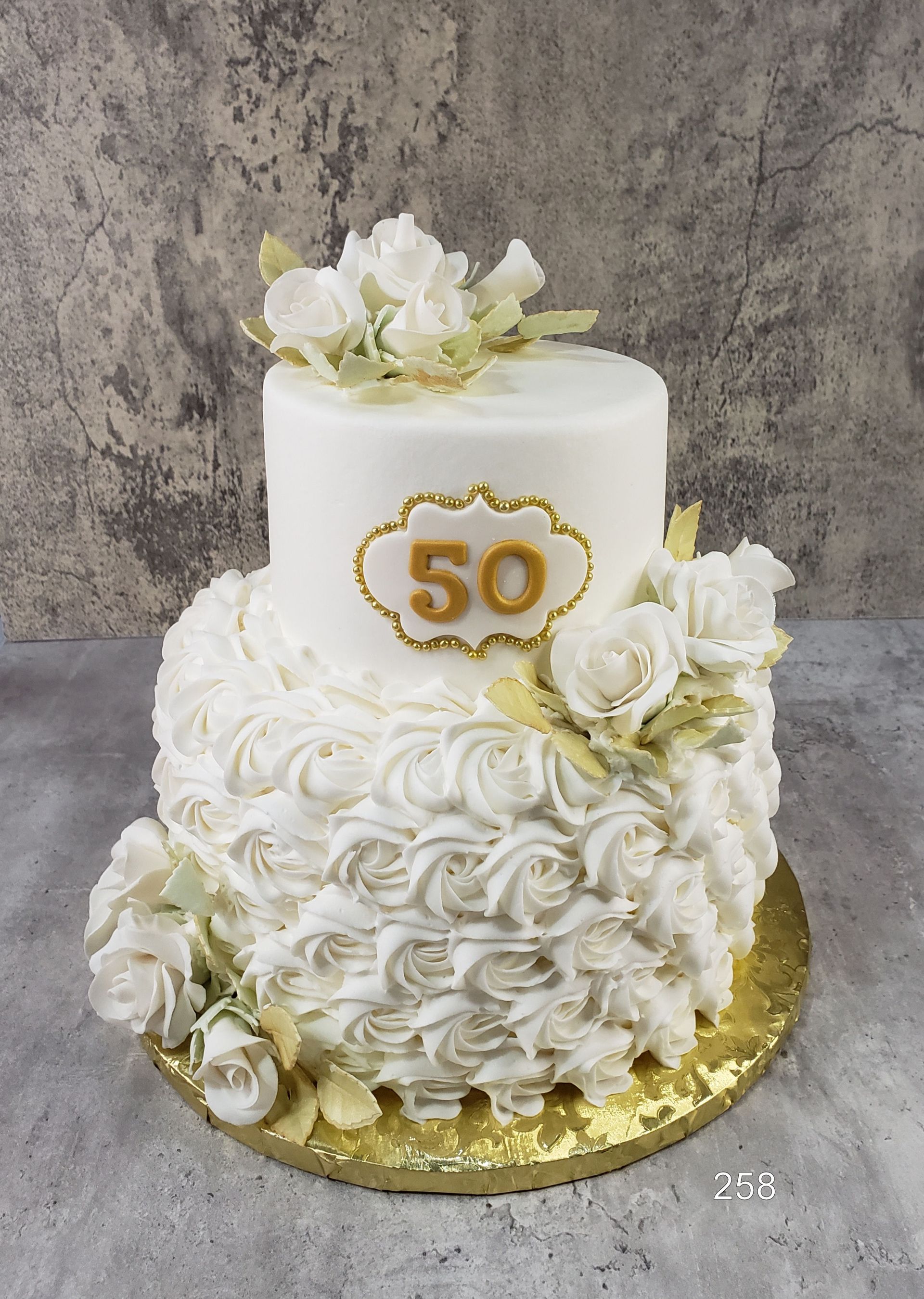 White and gold 50th anniversary cake with floral decorations on a gold board