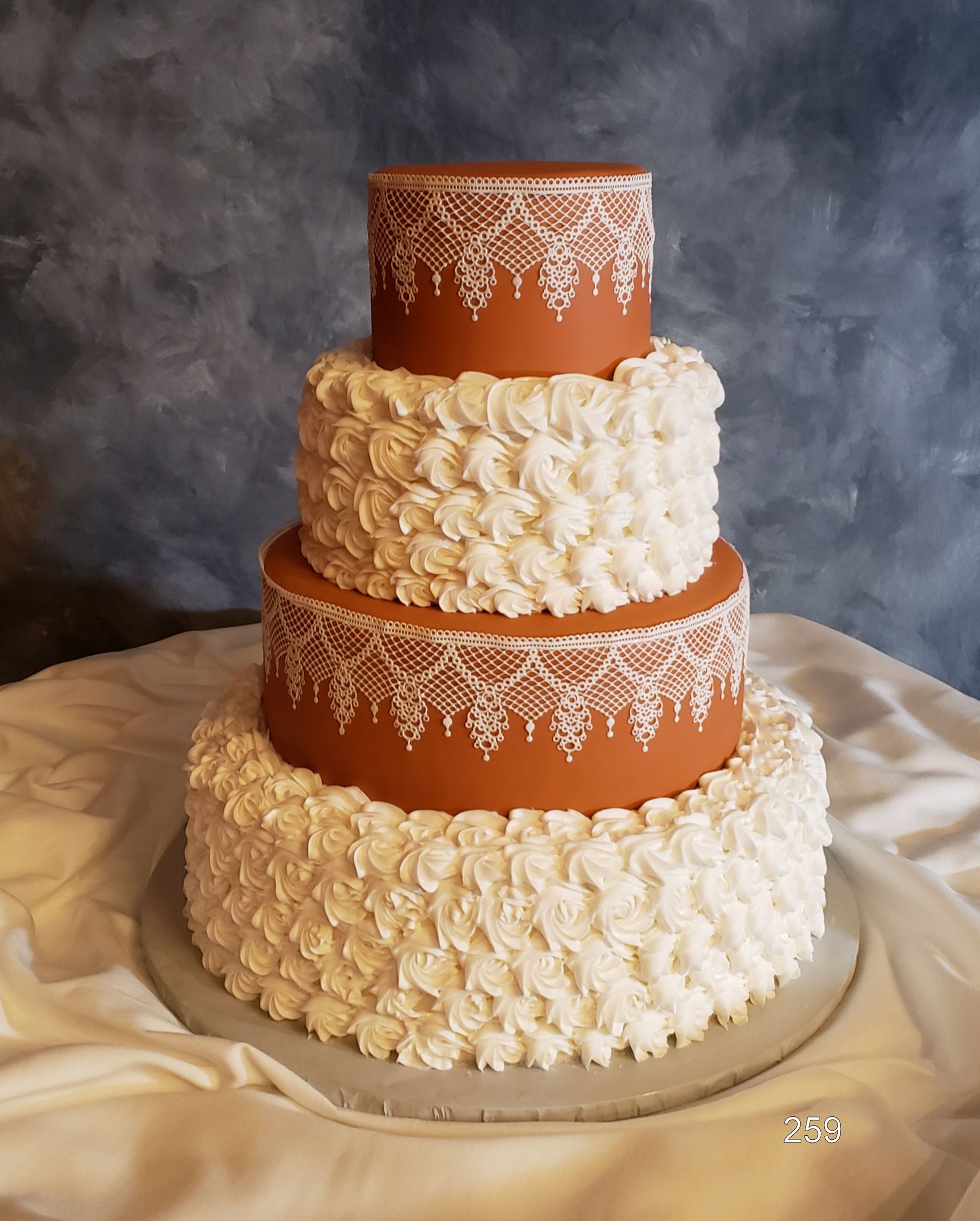 Tiered orange-and-white wedding cake with white floral piping on a draped table against a gray backdrop