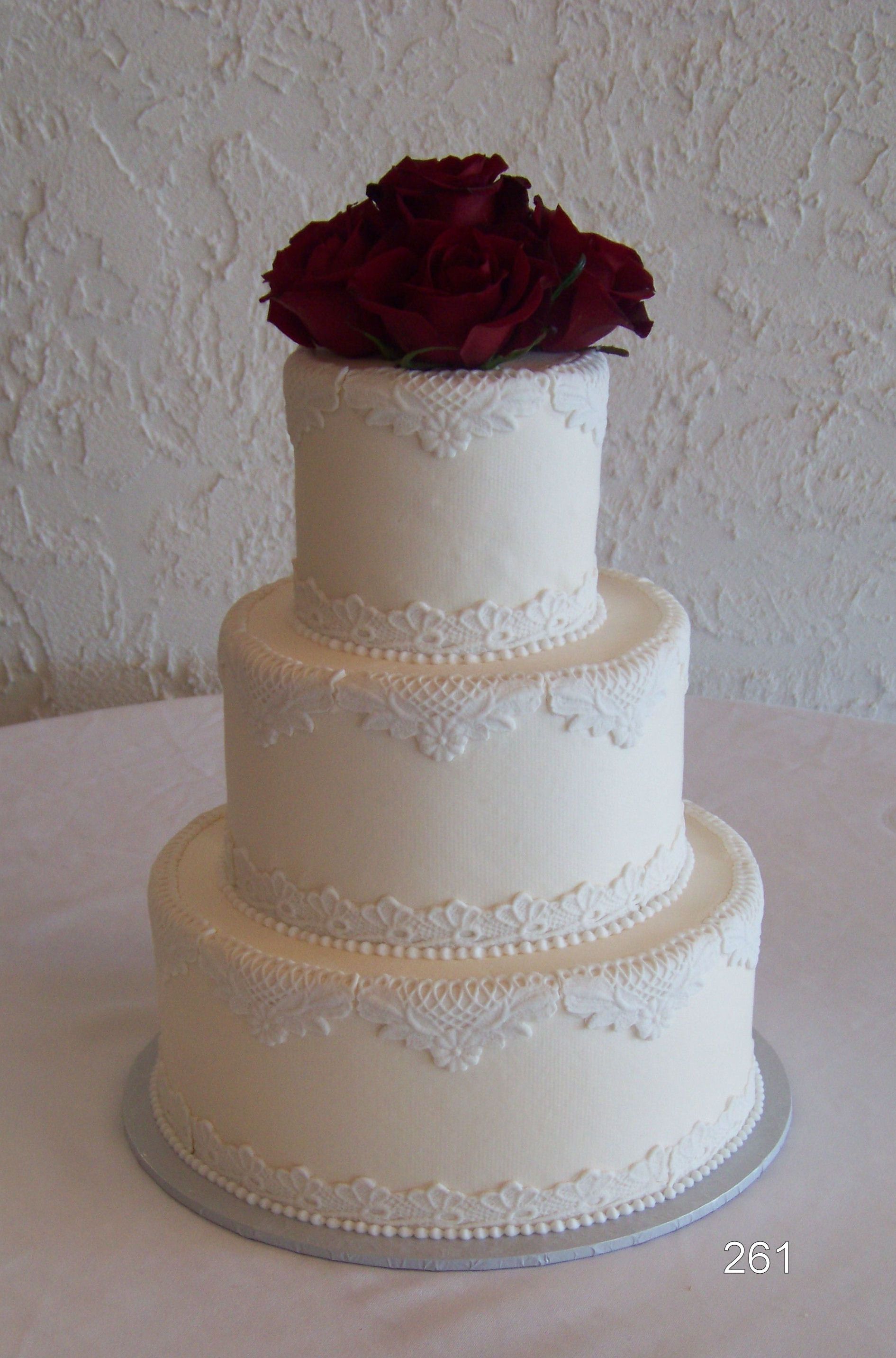 Three-tier white wedding cake with burgundy roses on top