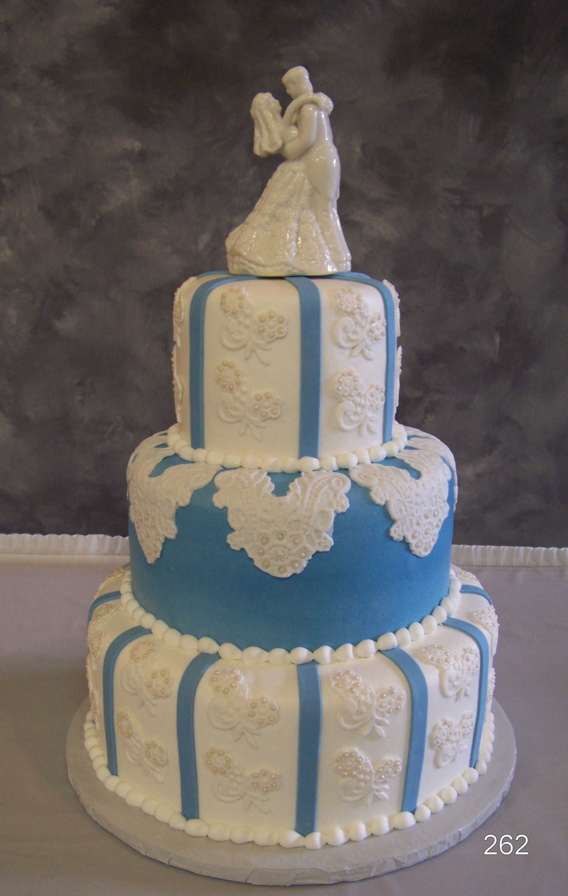 Three-tier white-and-blue decorated cake with a bride-and-groom topper on top