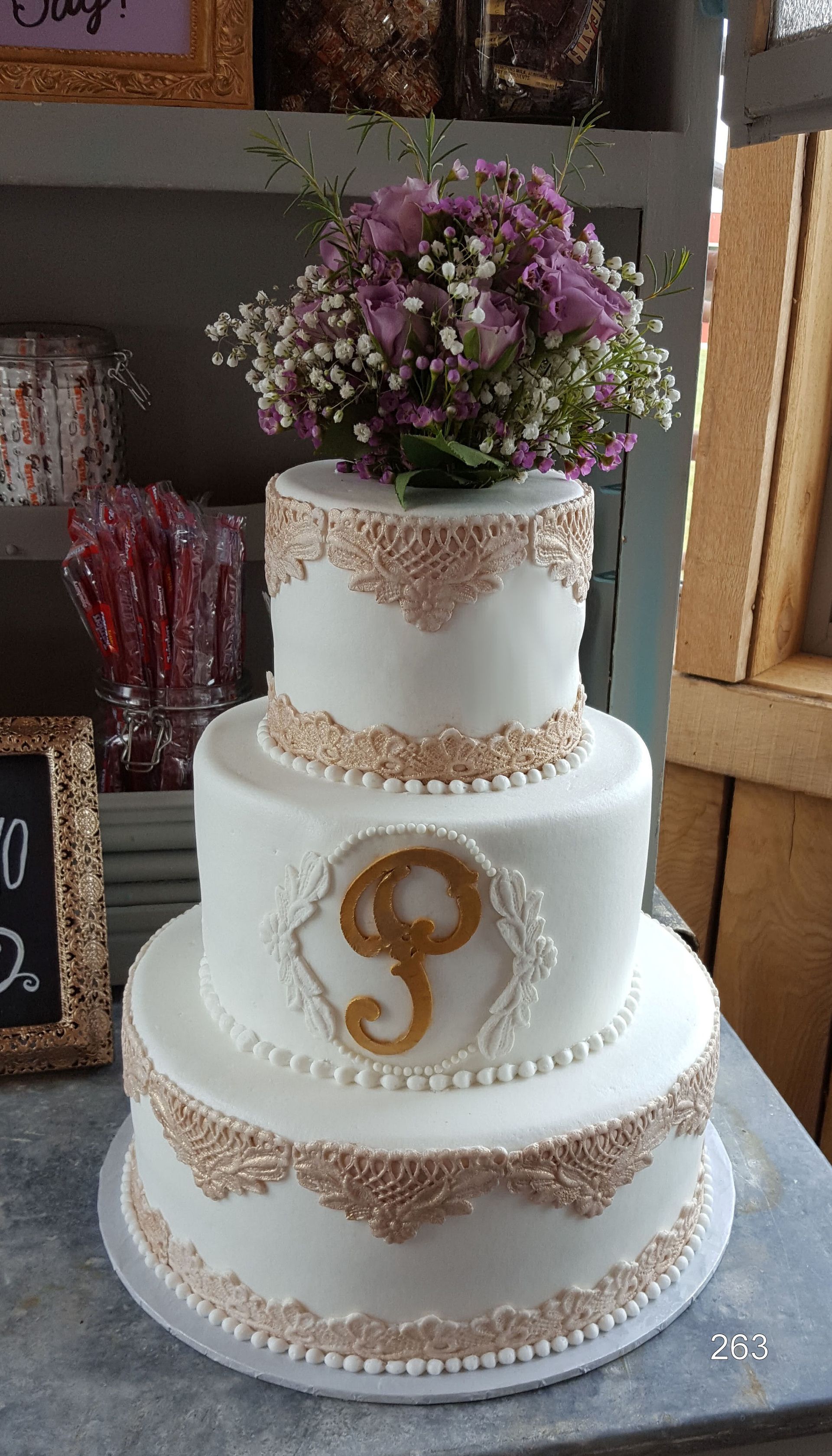 Three-tier white wedding cake with gold accents and purple flowers on top