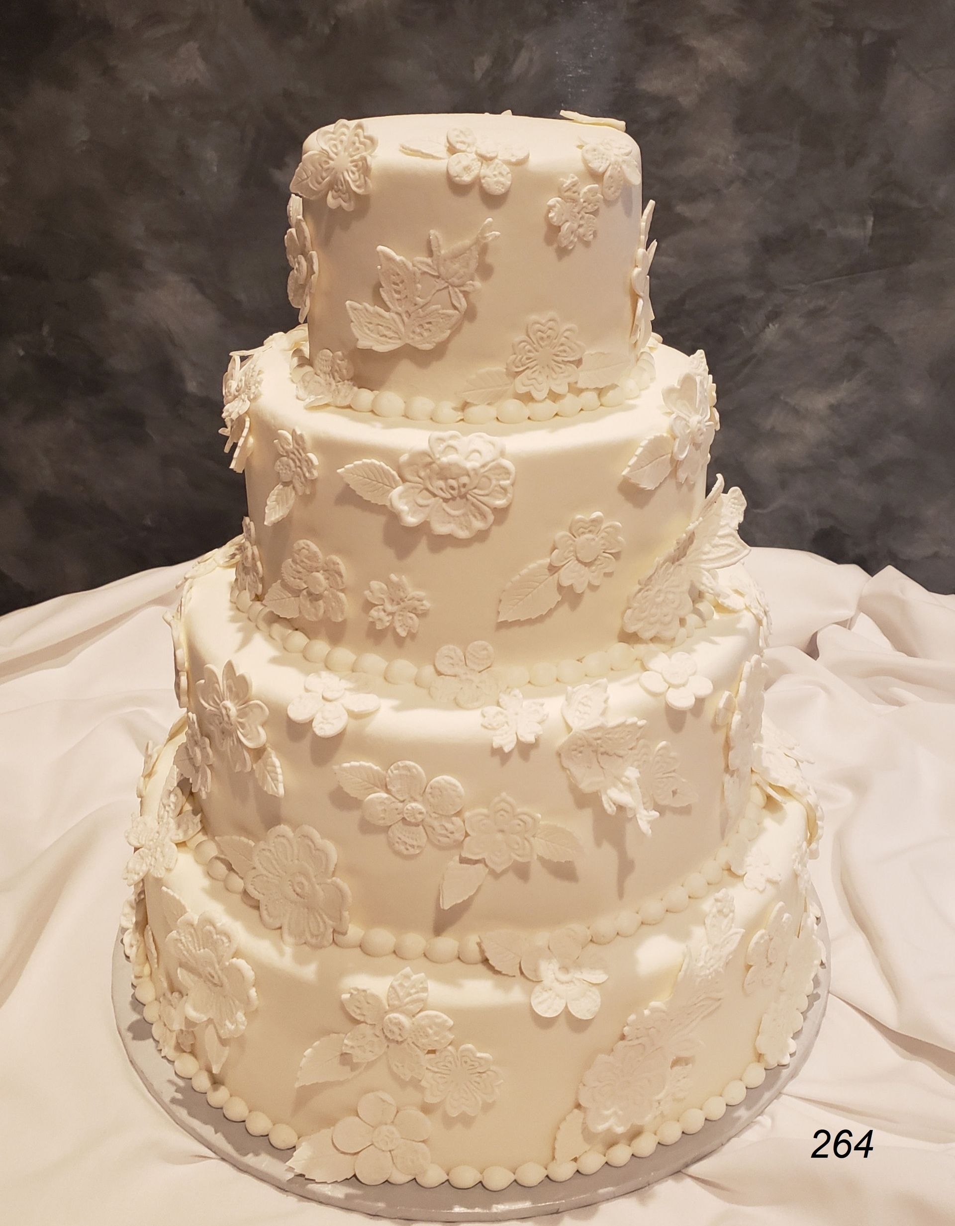 Four-tier white wedding cake with floral decorations and a draped fabric backdrop