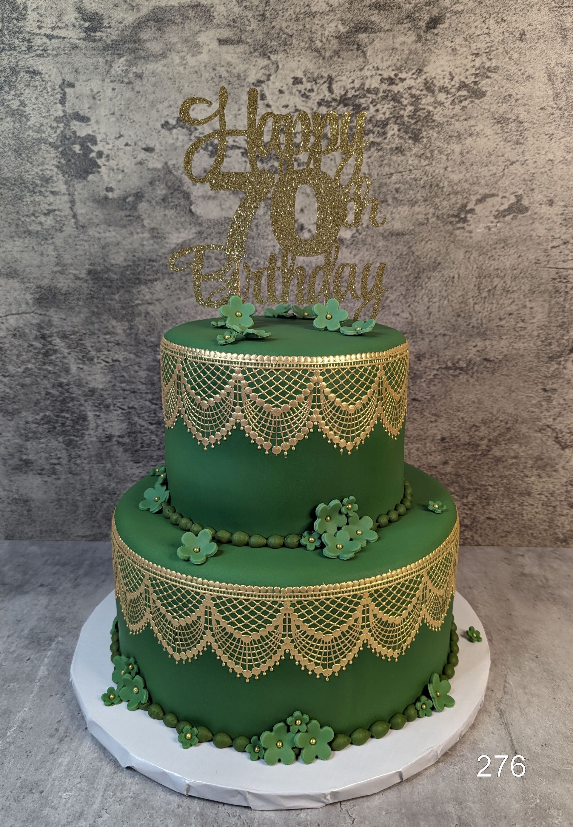 Two-tier green cake with gold lace trim and “Happy Eid” topper on a white board