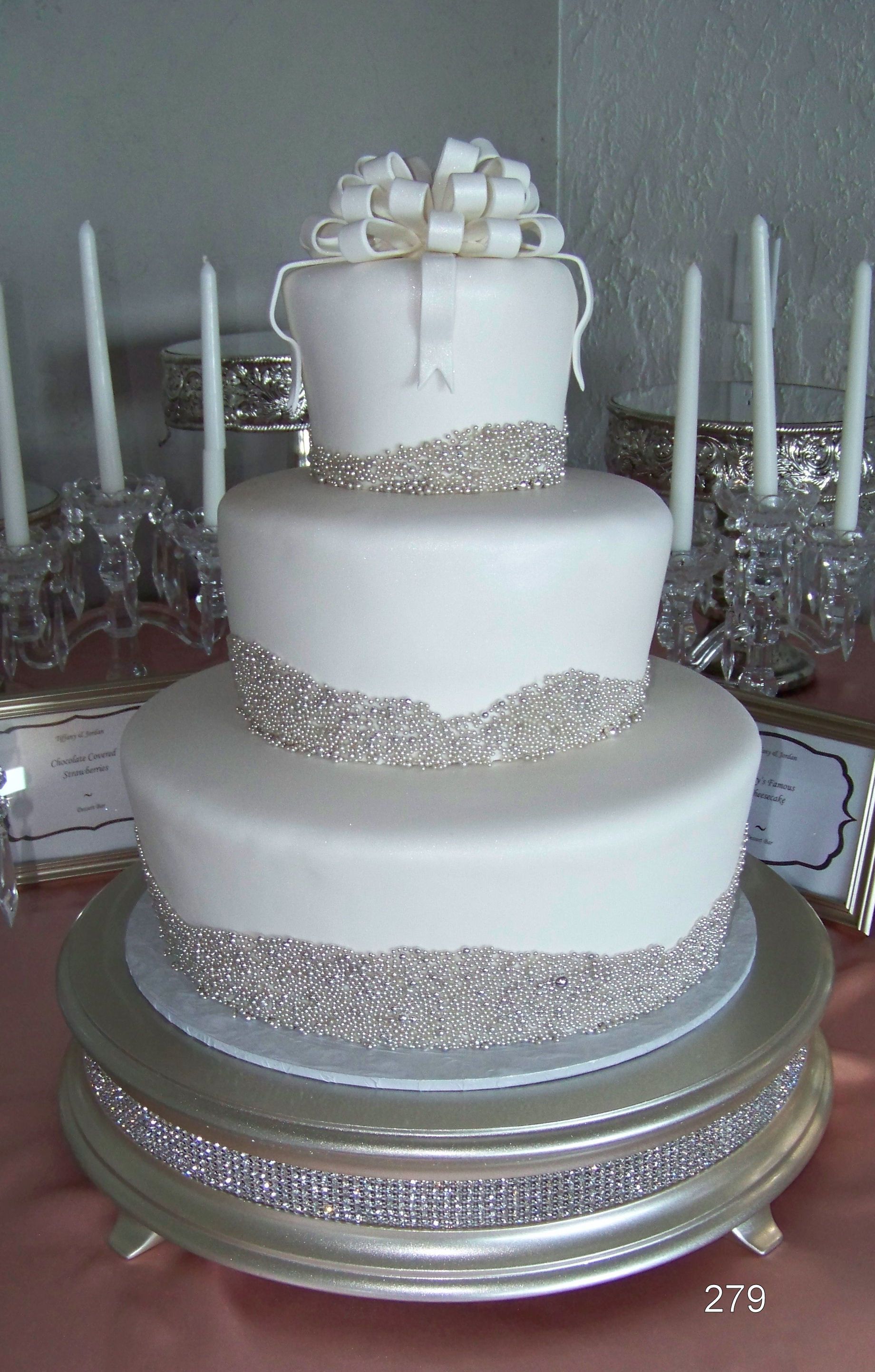 Three-tier white wedding cake with silver trim on a decorated table