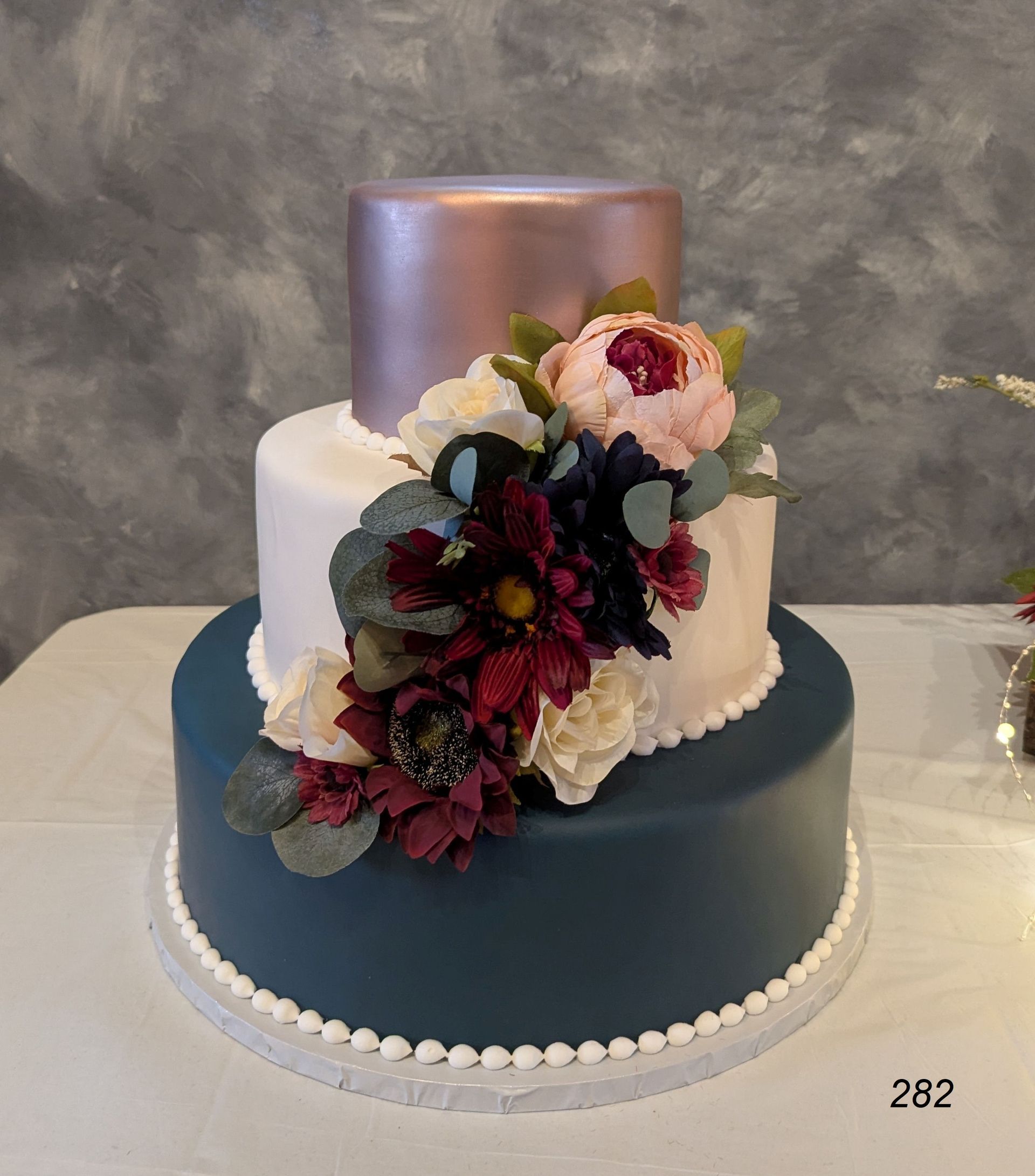 Two-tier blue and white cake with pink and dark floral decorations and a metallic topper