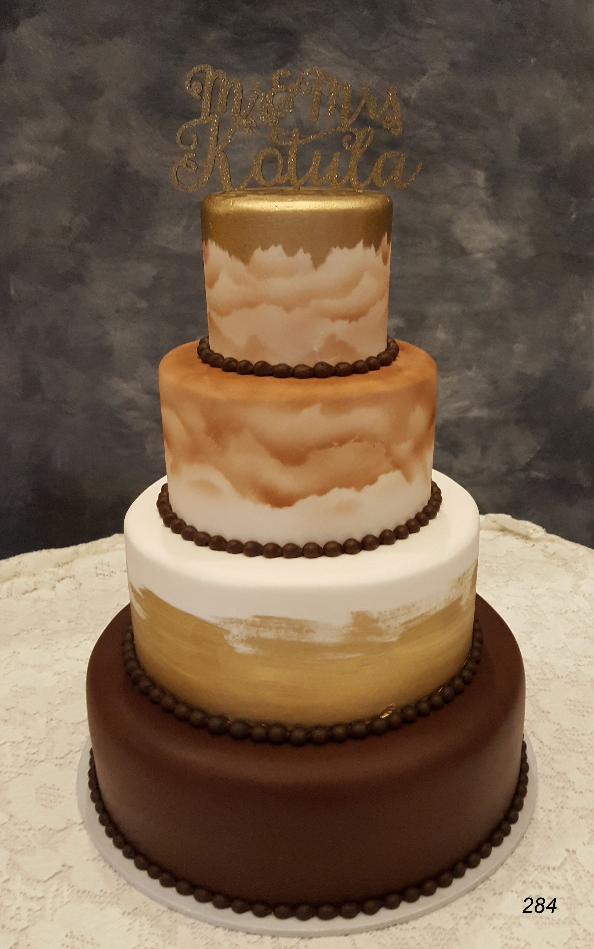 Four-tiered wedding cake with gold and white marble accents and a gold topper, on a gray backdrop