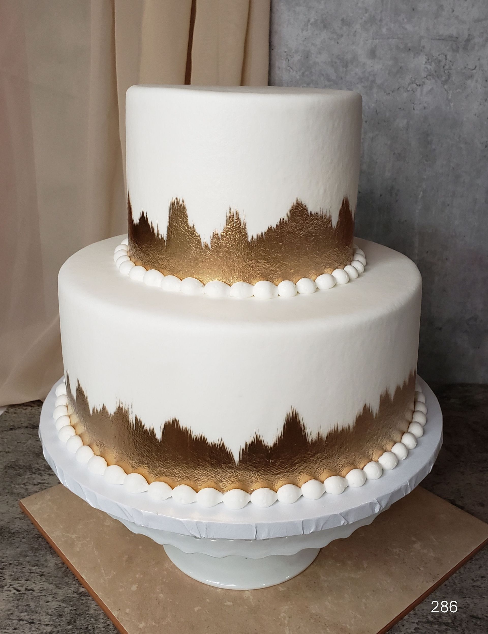 Two-tier white wedding cake with gold leaf accents on a cake stand