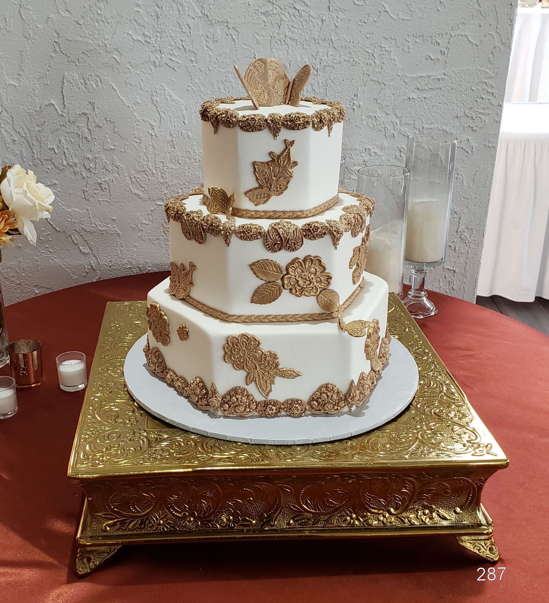 Three-tier white cake with gold floral accents on a gold stand at a decorated event table