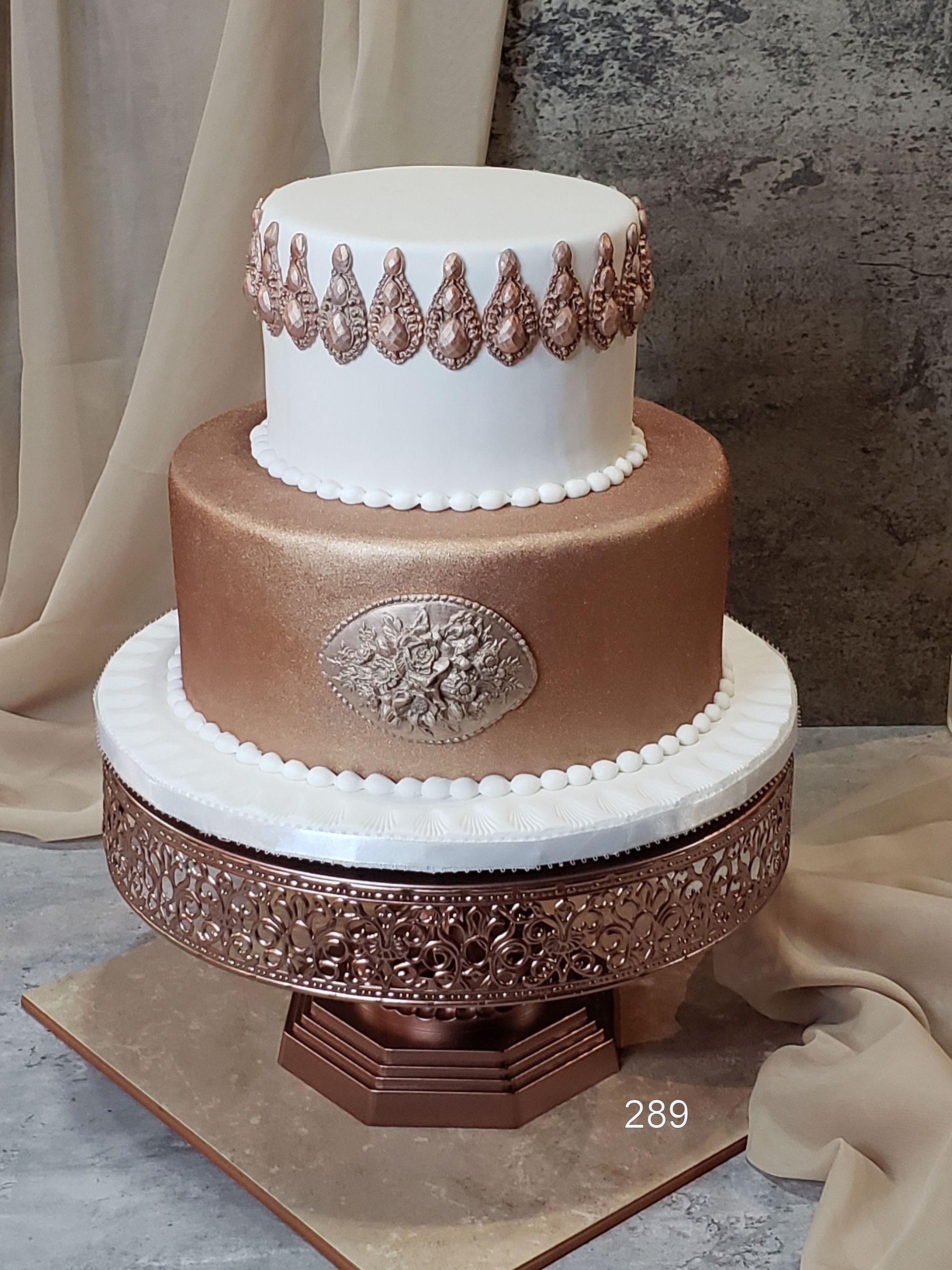 Three-tier white and rose-gold wedding cake with jeweled details on a decorative stand