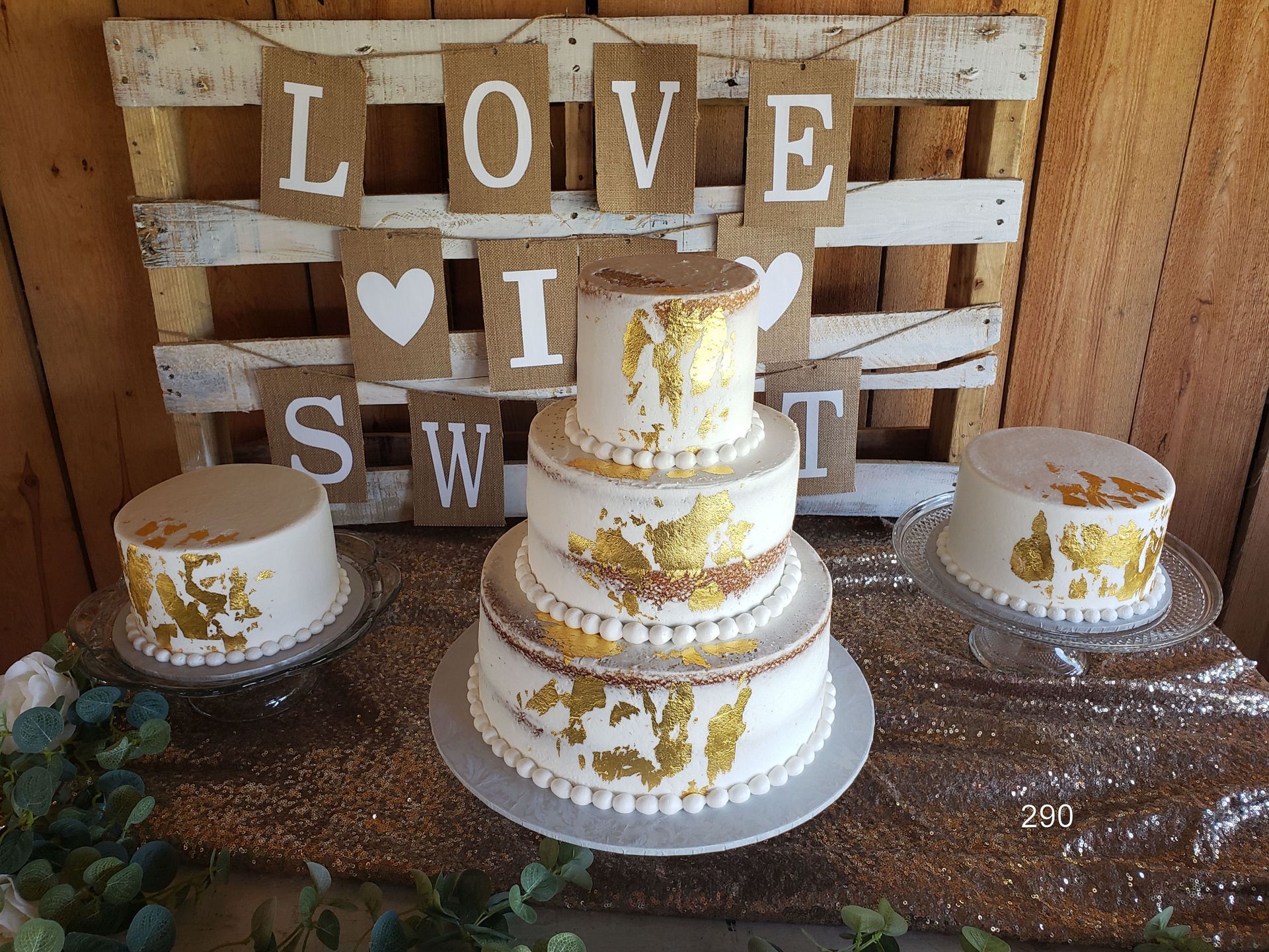 Rustic wedding dessert table with three white-and-gold cakes and “LOVE” wooden blocks backdrop