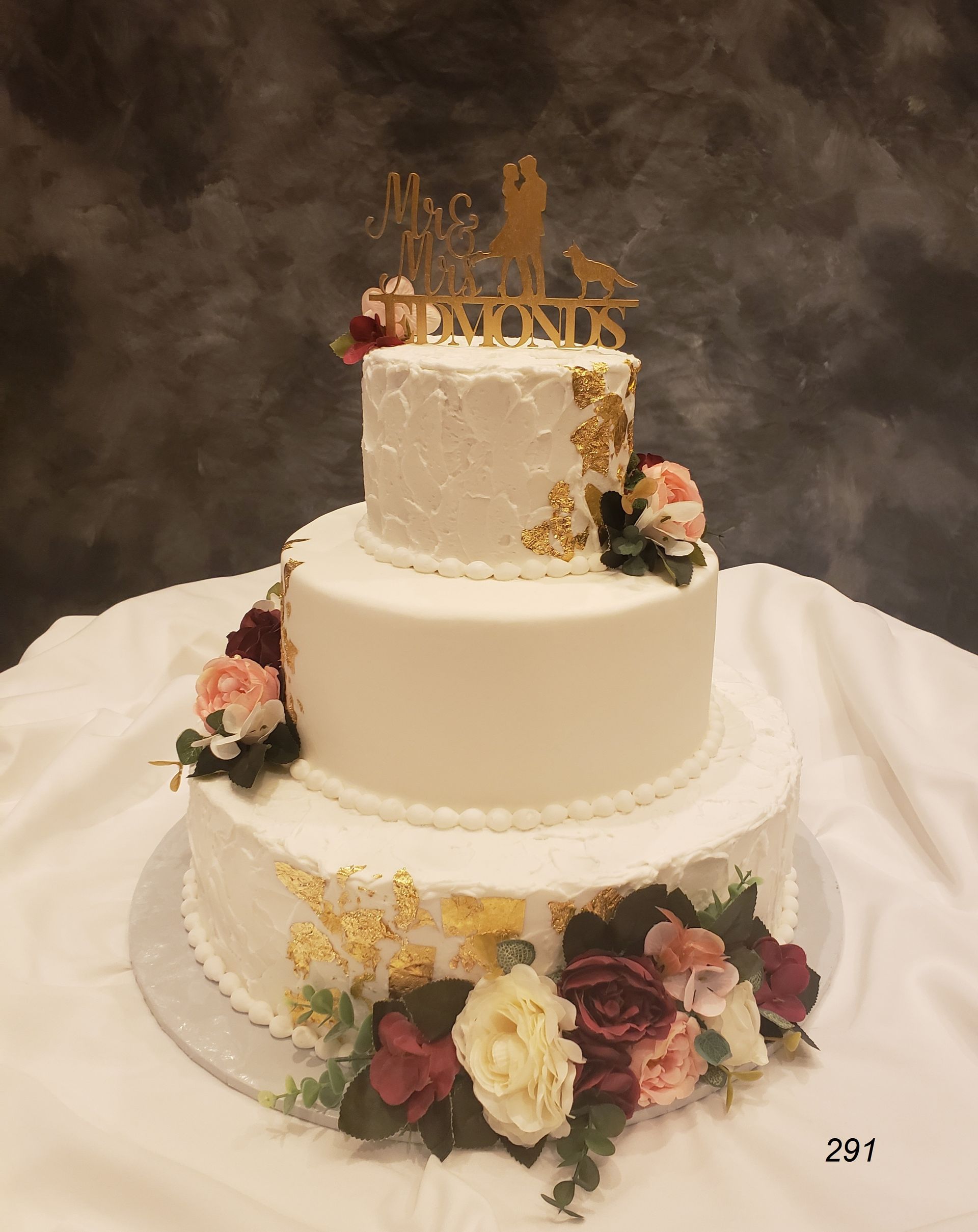 Three-tier white wedding cake with gold topper and pink, white, and yellow flowers