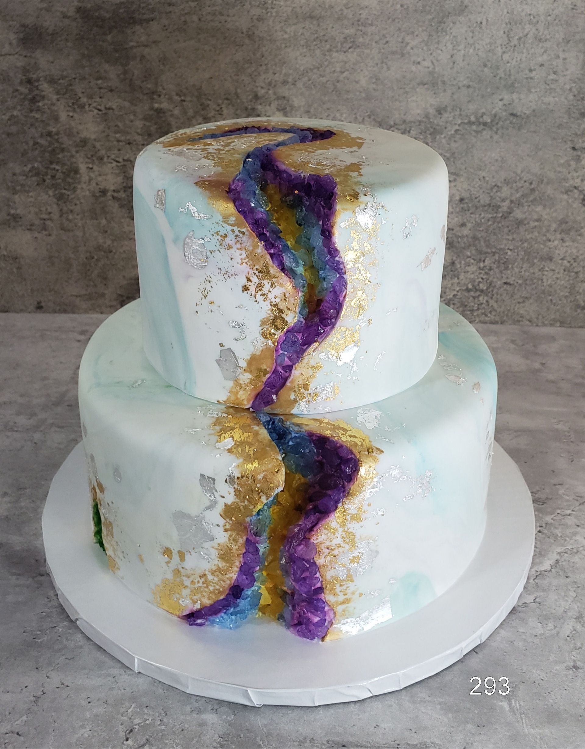 Two-tier white cake with purple and gold wavy decoration on a round white board