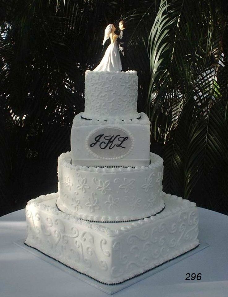 White three-tier wedding cake with ornate icing and a bride-and-groom topper outdoors at night