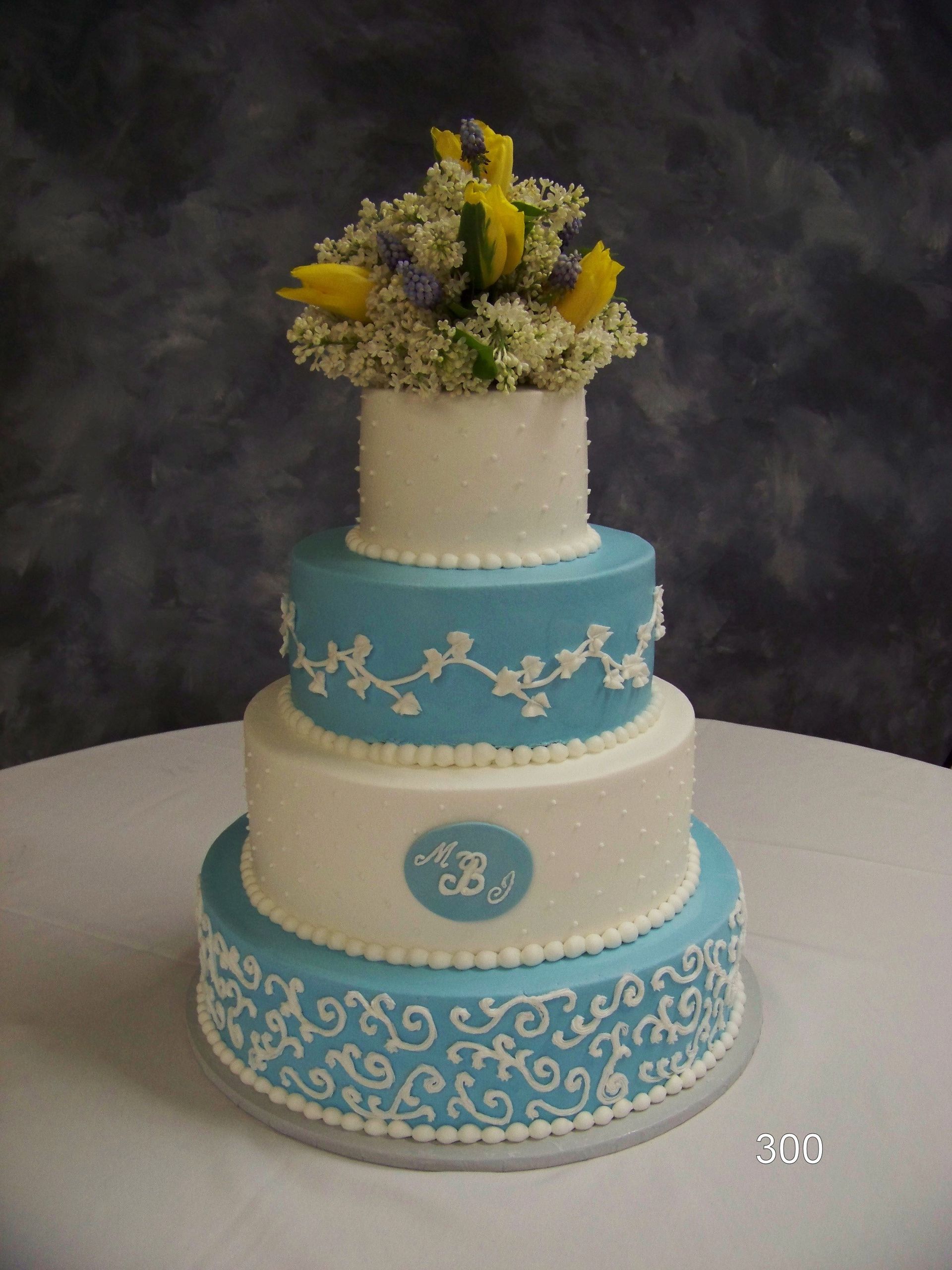Three-tiered blue and white decorative cake with floral top, on a dark backdrop