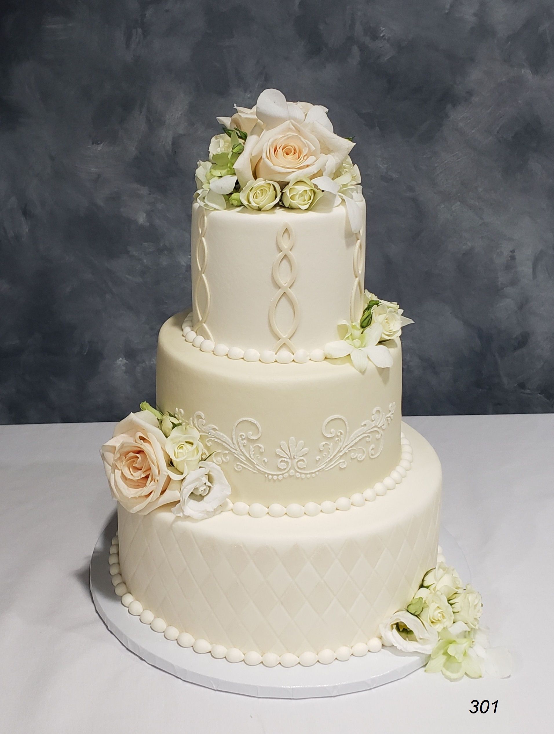 Three-tier white wedding cake with cream flowers and pearl-like trim on a white stand