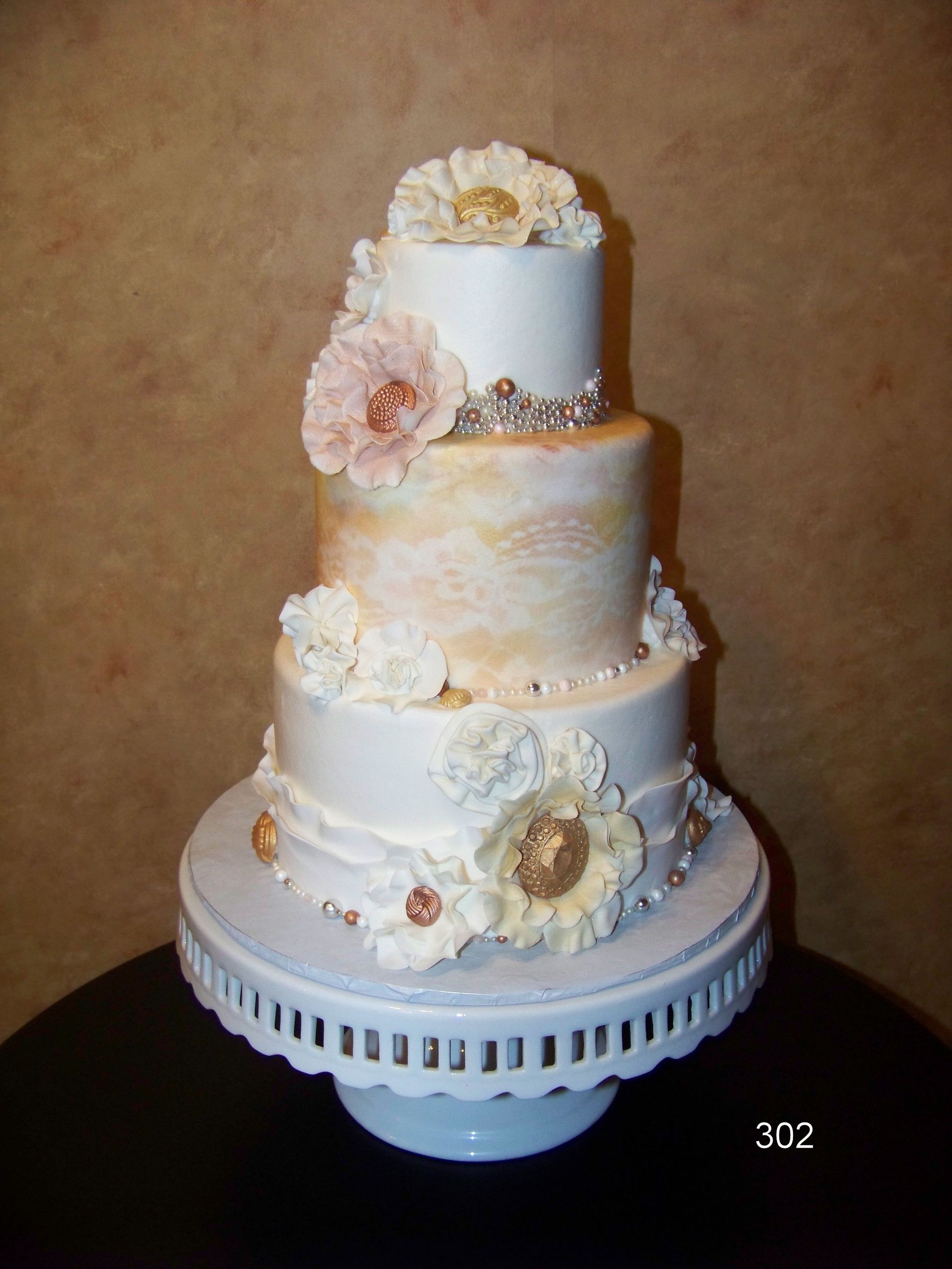Four-tier white and cream wedding cake with floral decorations on a white pedestal stand